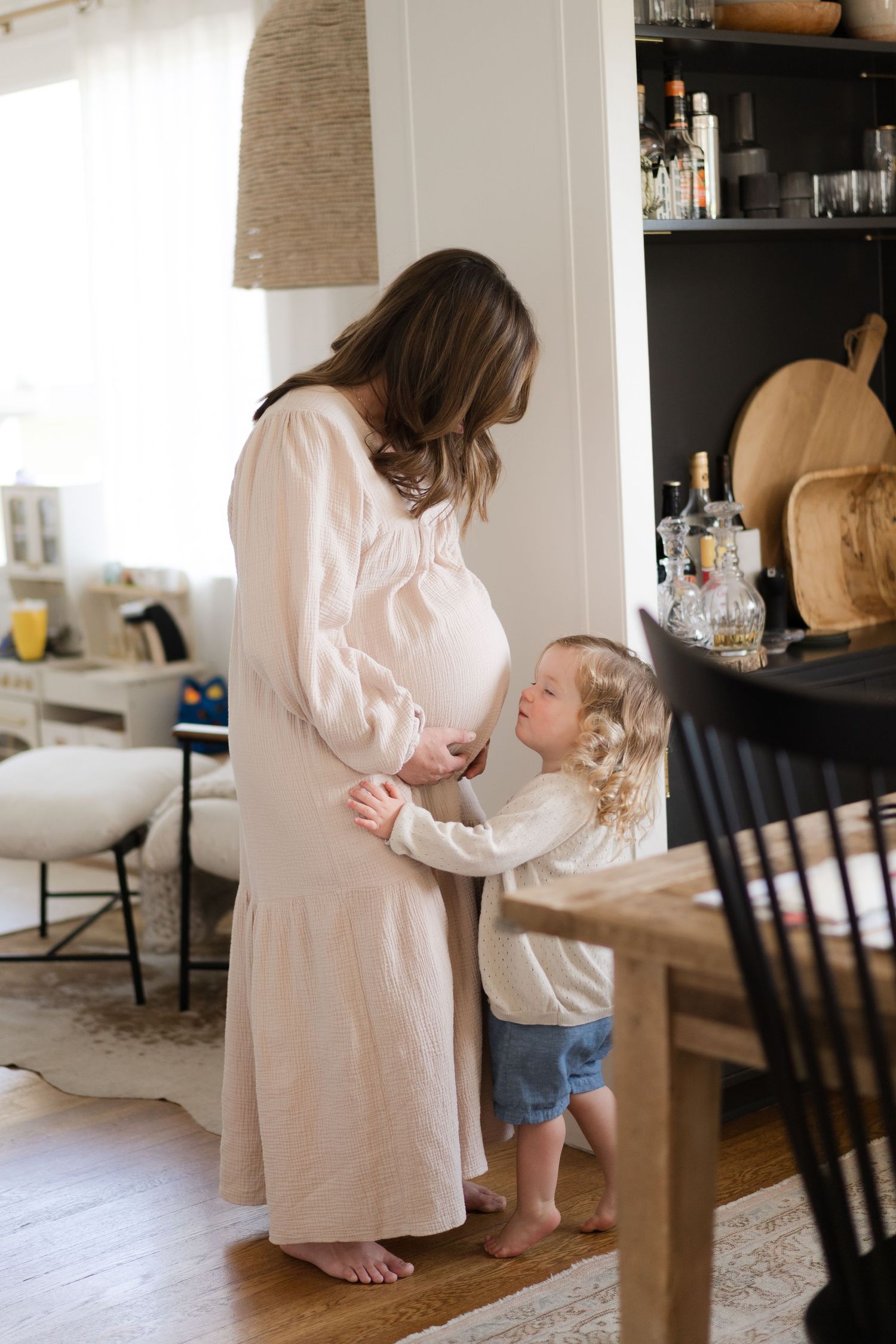 Mother and child share tender moment in sunlit living room with modern decor.
