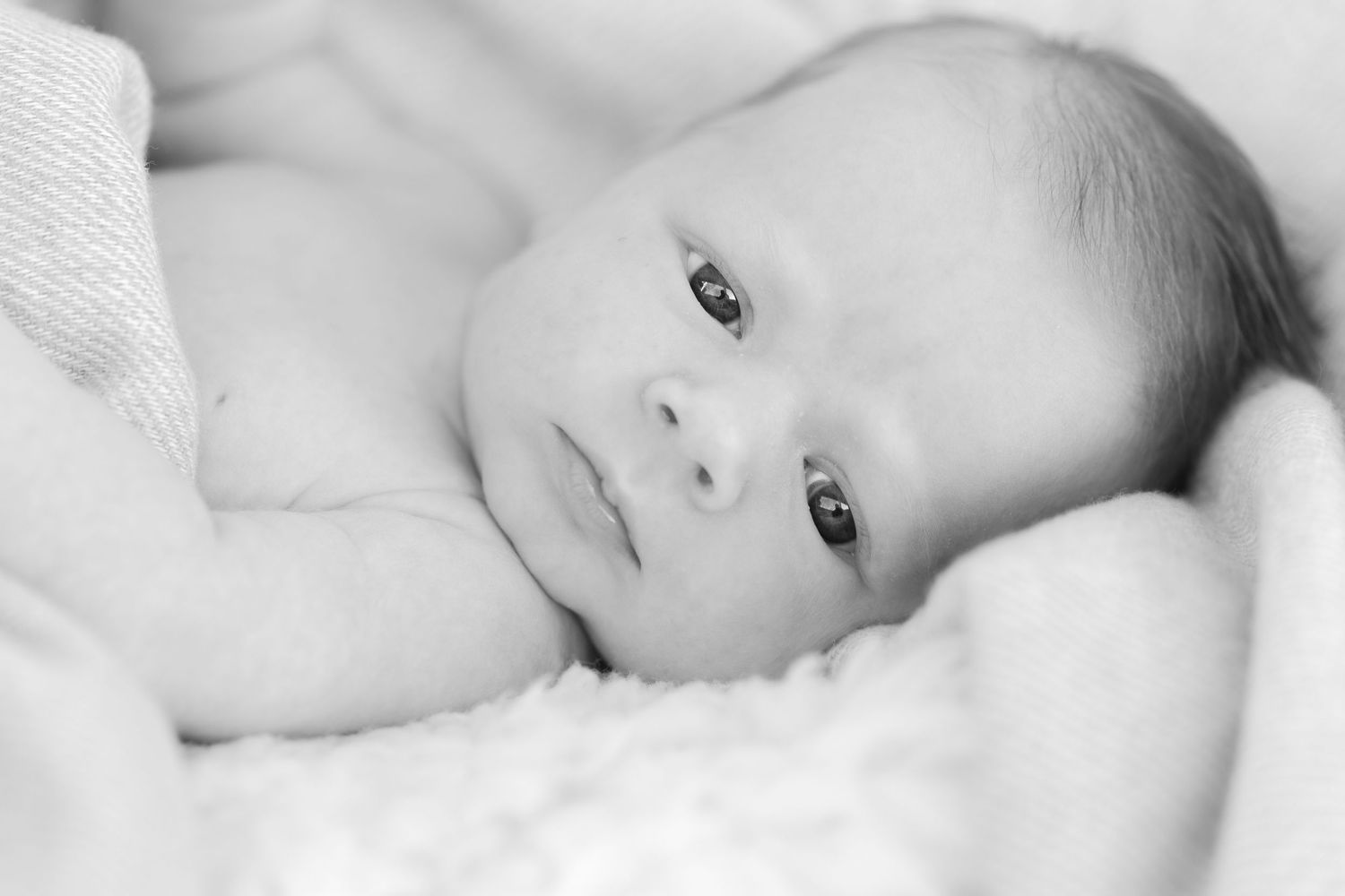 Black and white series of a baby lying on white bedding.