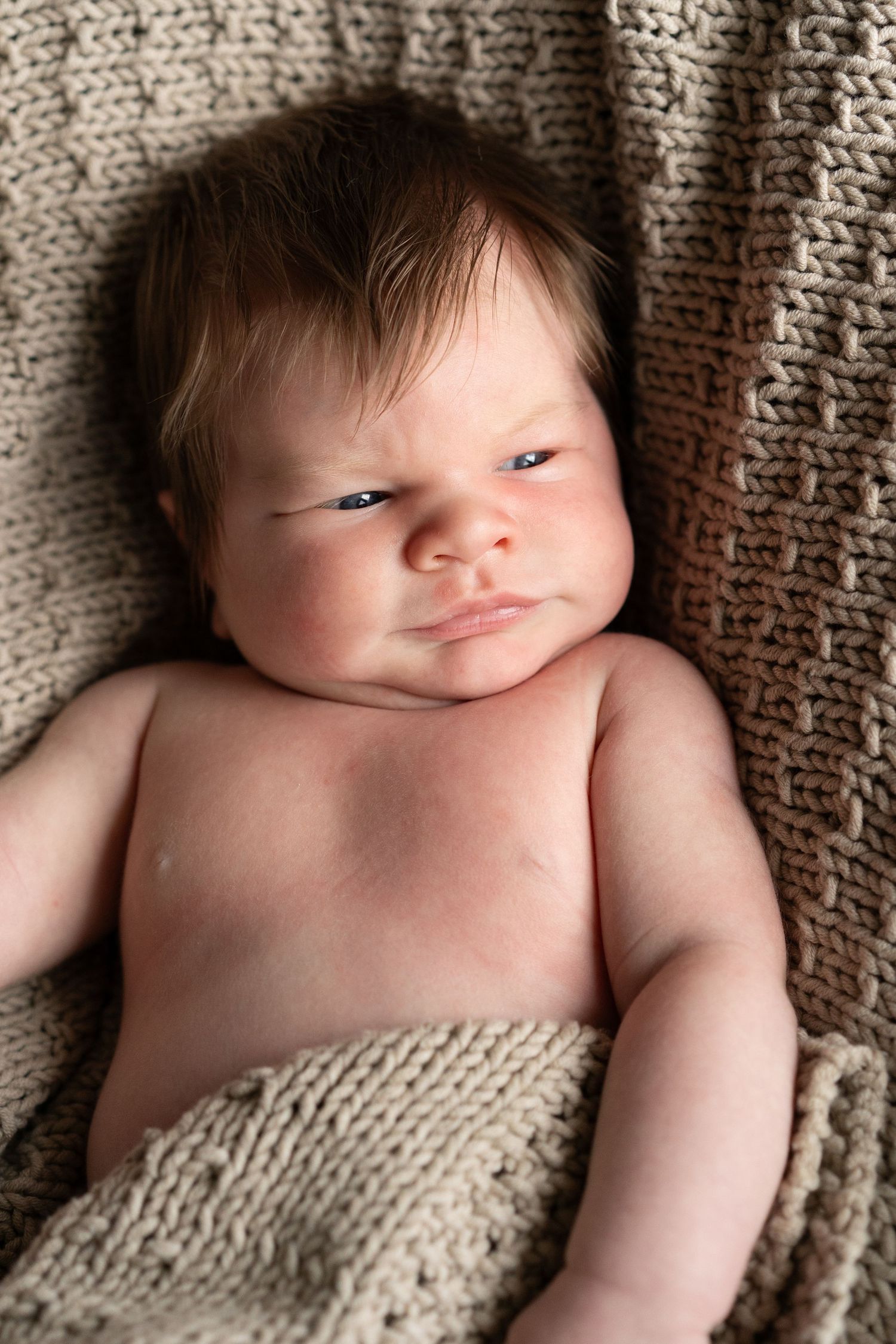 Newborn baby with dark hair lying on knit blanket in progressive expressions.
