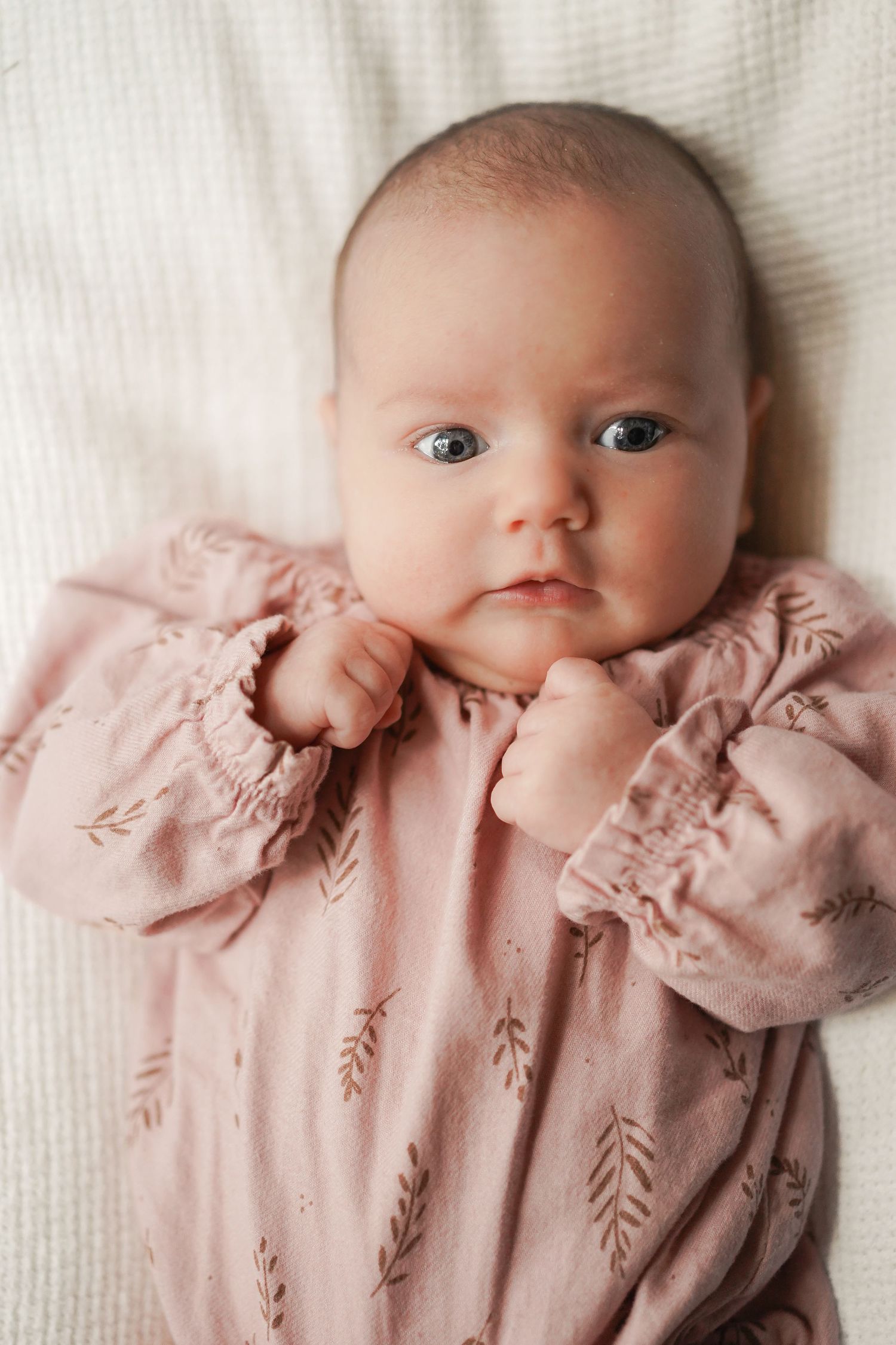 Baby in pink patterned romper with puffy sleeves lying on white fabric.