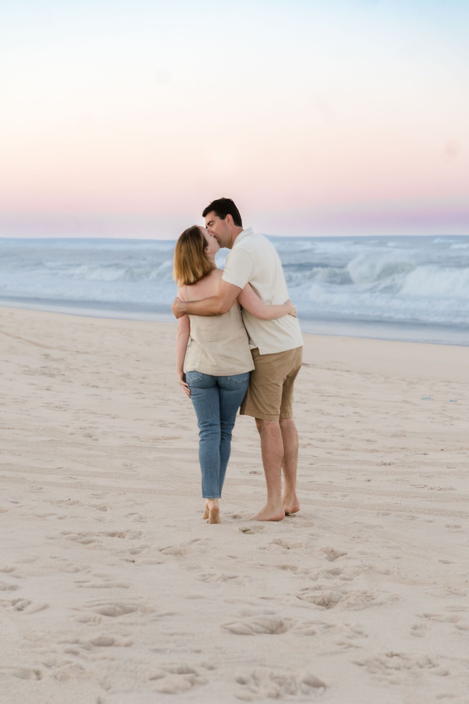 Romantic couple embracing while walking along the shoreline at dusk.