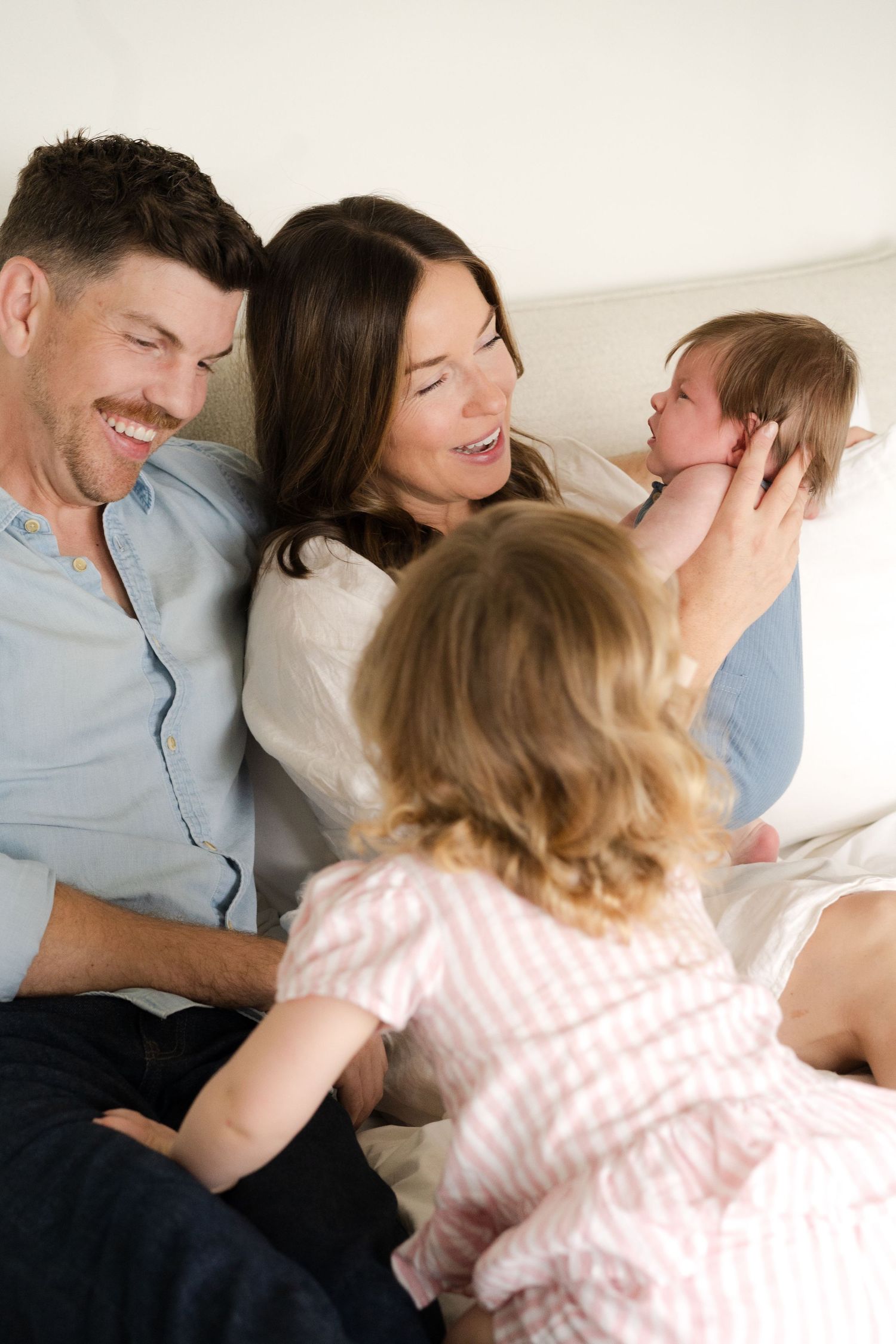 Family sharing joyful cuddles and laughter together on white bedding.