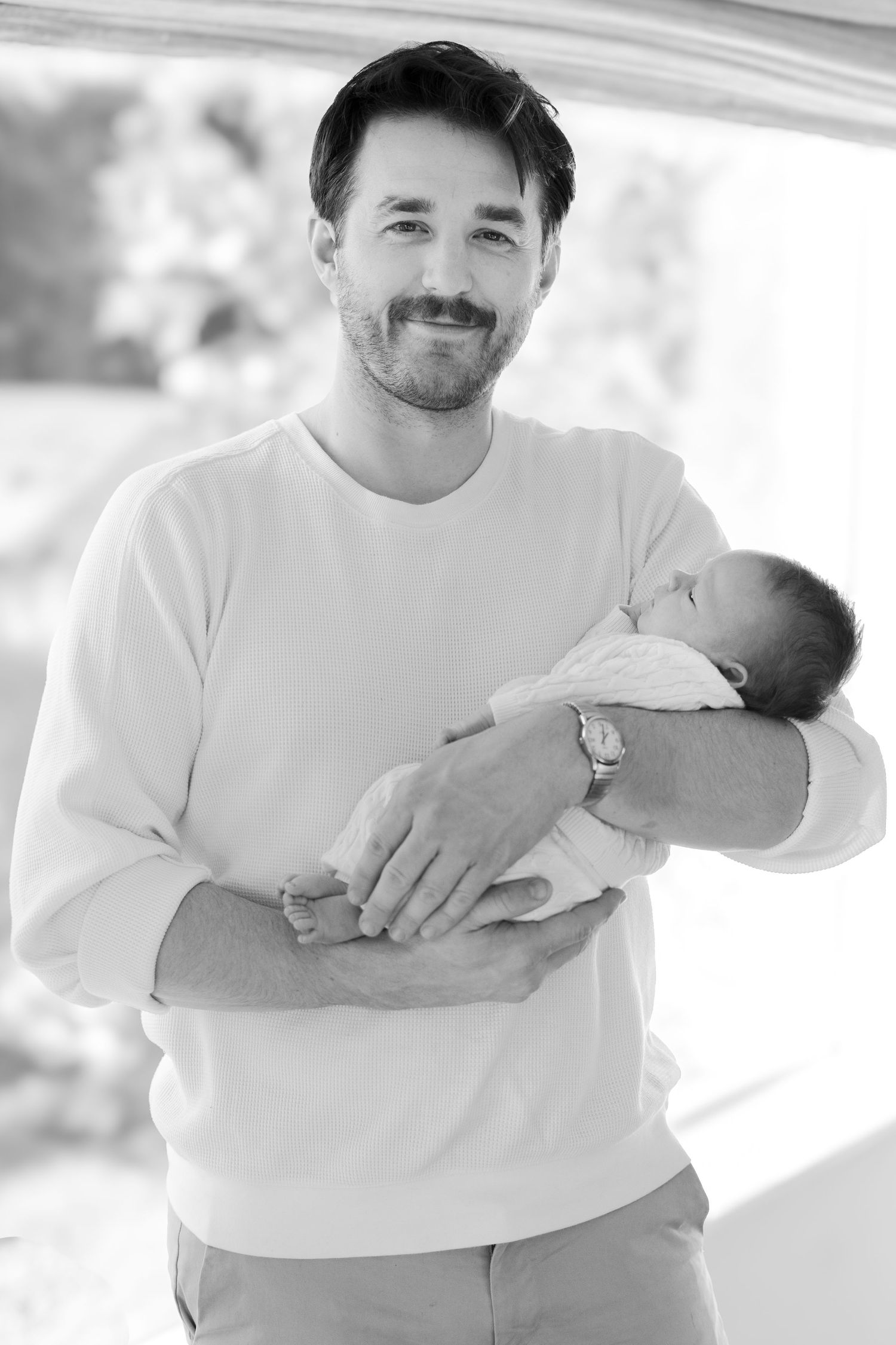 Black and white portrait of person in white sweater cradling sleeping newborn.