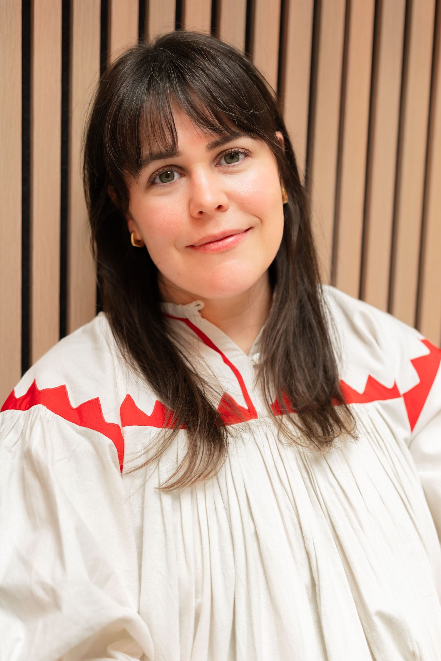 A person in a white collared shirt with red zigzag trim poses in a triptych against a wooden slat background.