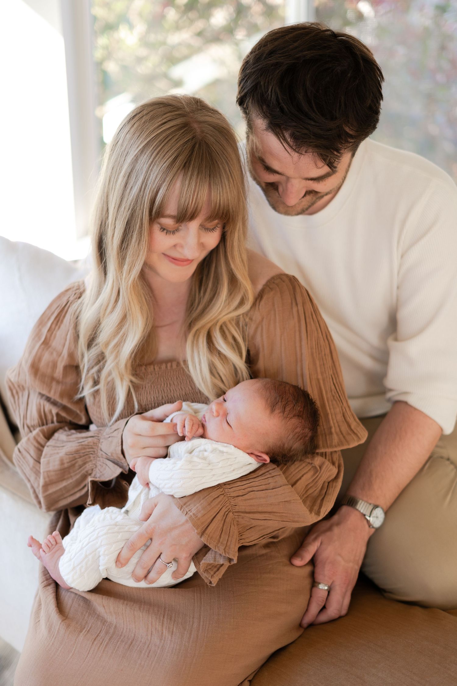 Intimate family portraits showing parents snuggling with their newborn baby on a brown couch.