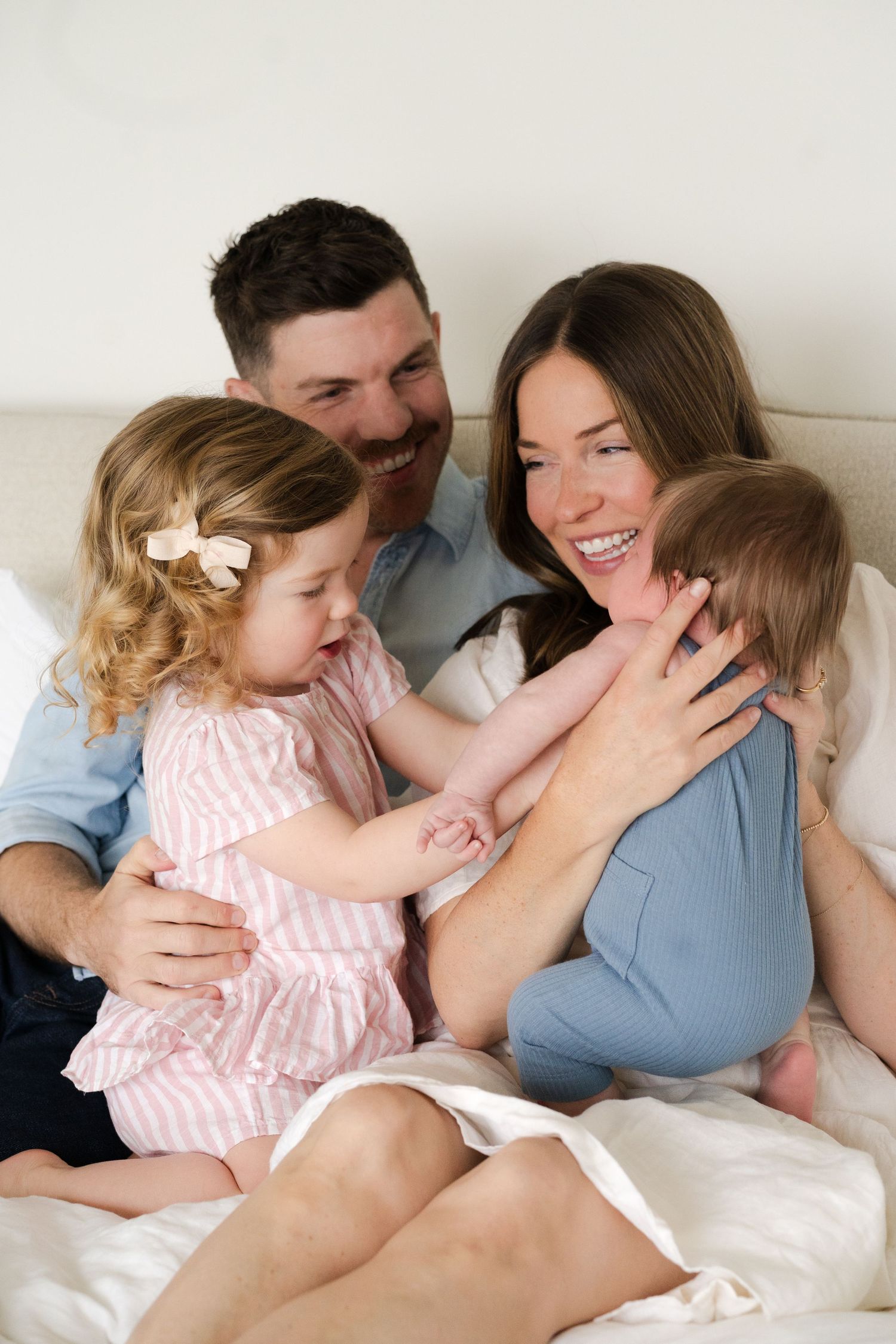 Candid family photo showing playful interaction and genuine smiles on white bedding.