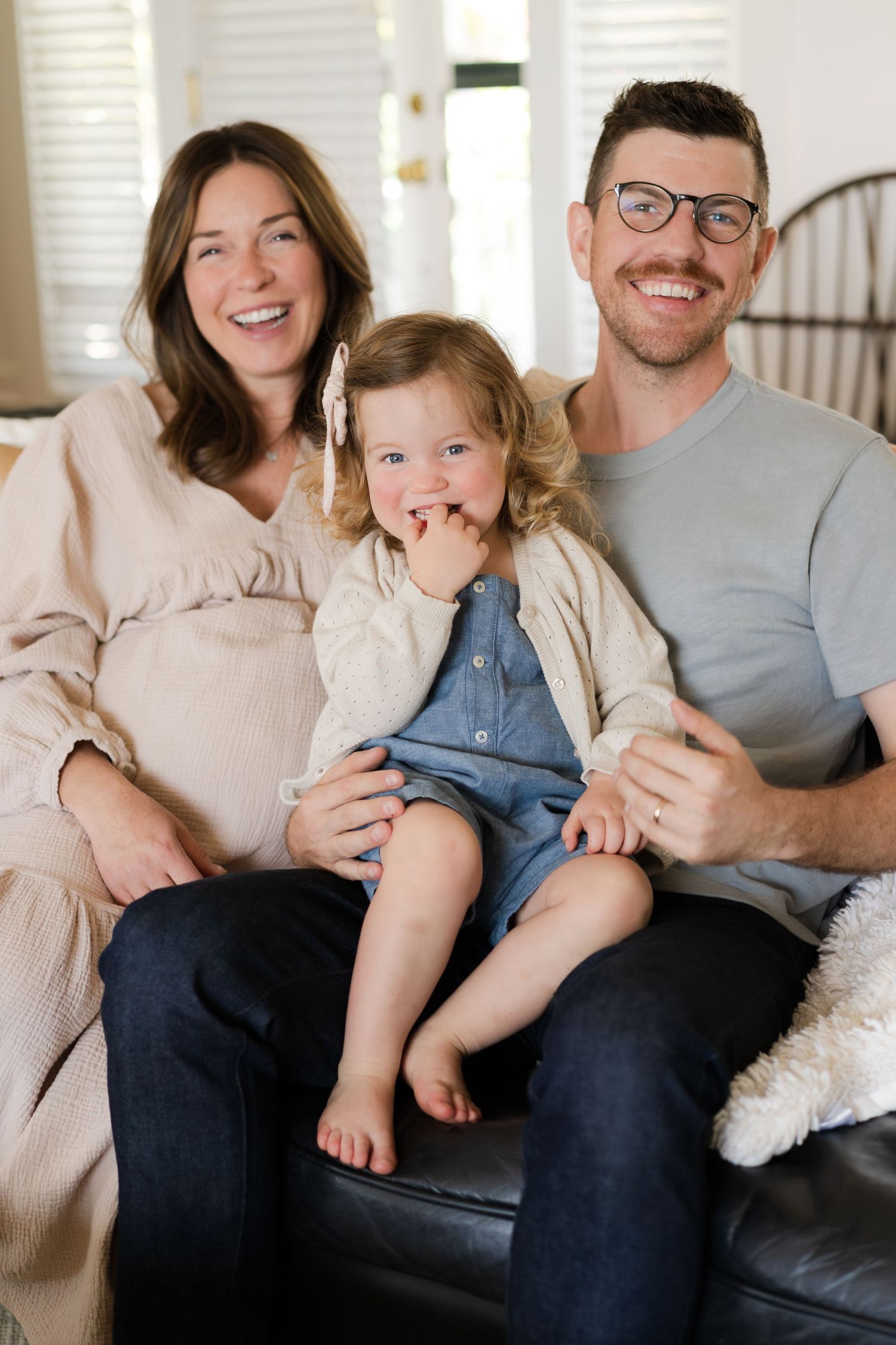 Family relaxing together on a dark leather couch in a bright living room with white walls.