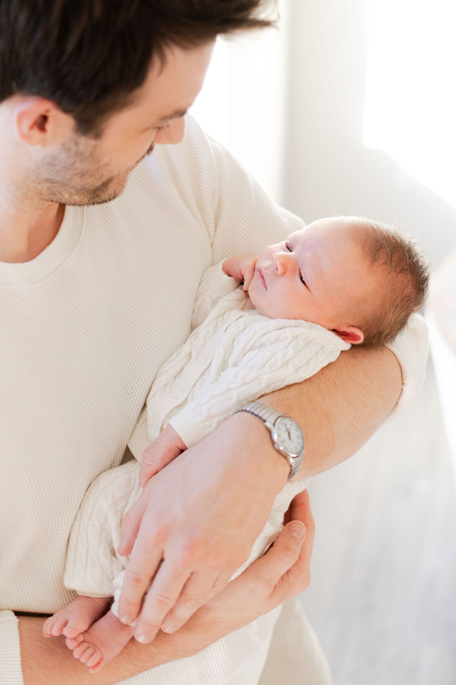 Intimate close-up of parent holding sleeping newborn baby in white onesie.