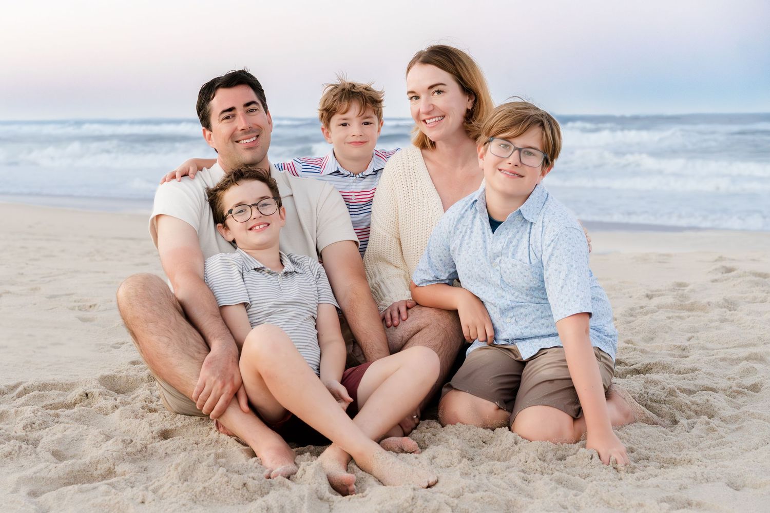 A family of five sitting together on a sandy beach at sunset.