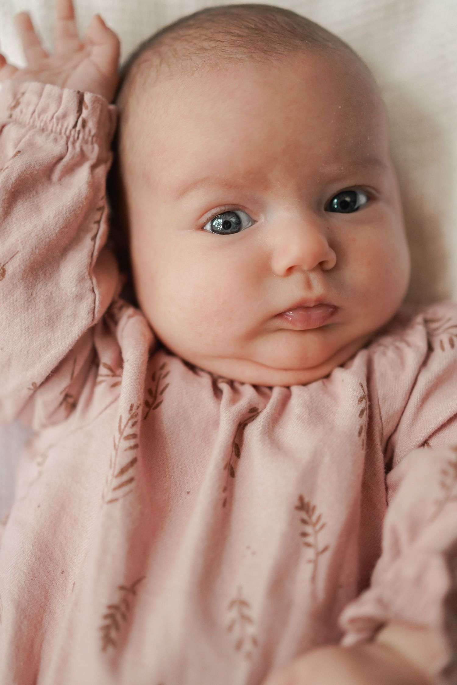 Close-up portrait of baby in pink leaf-patterned outfit against white background.