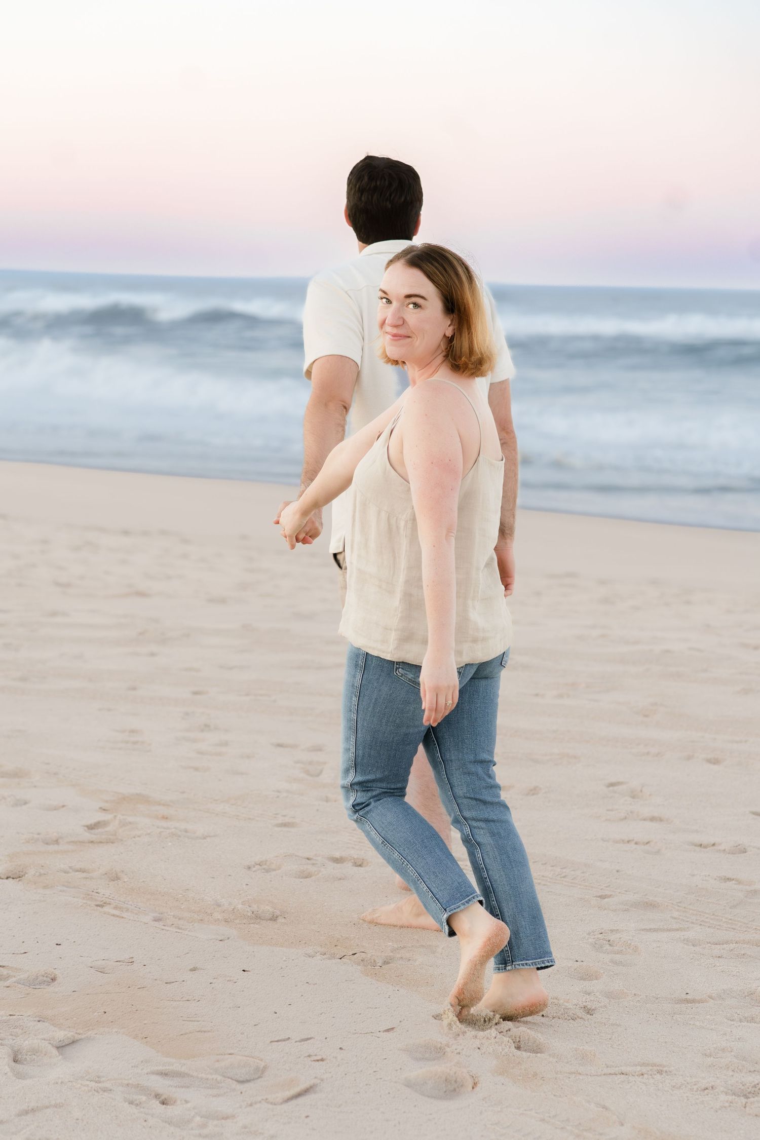 Couple playfully running and leaving footprints in the sand at sunset on a peaceful beach.