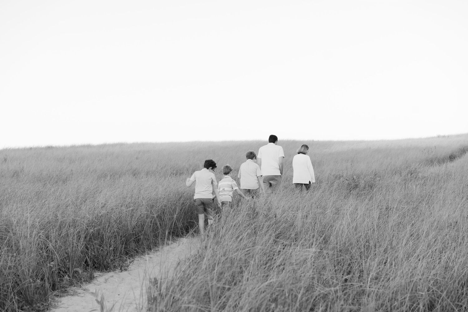 Black and white image of a family walking through tall grass on a coastal path.