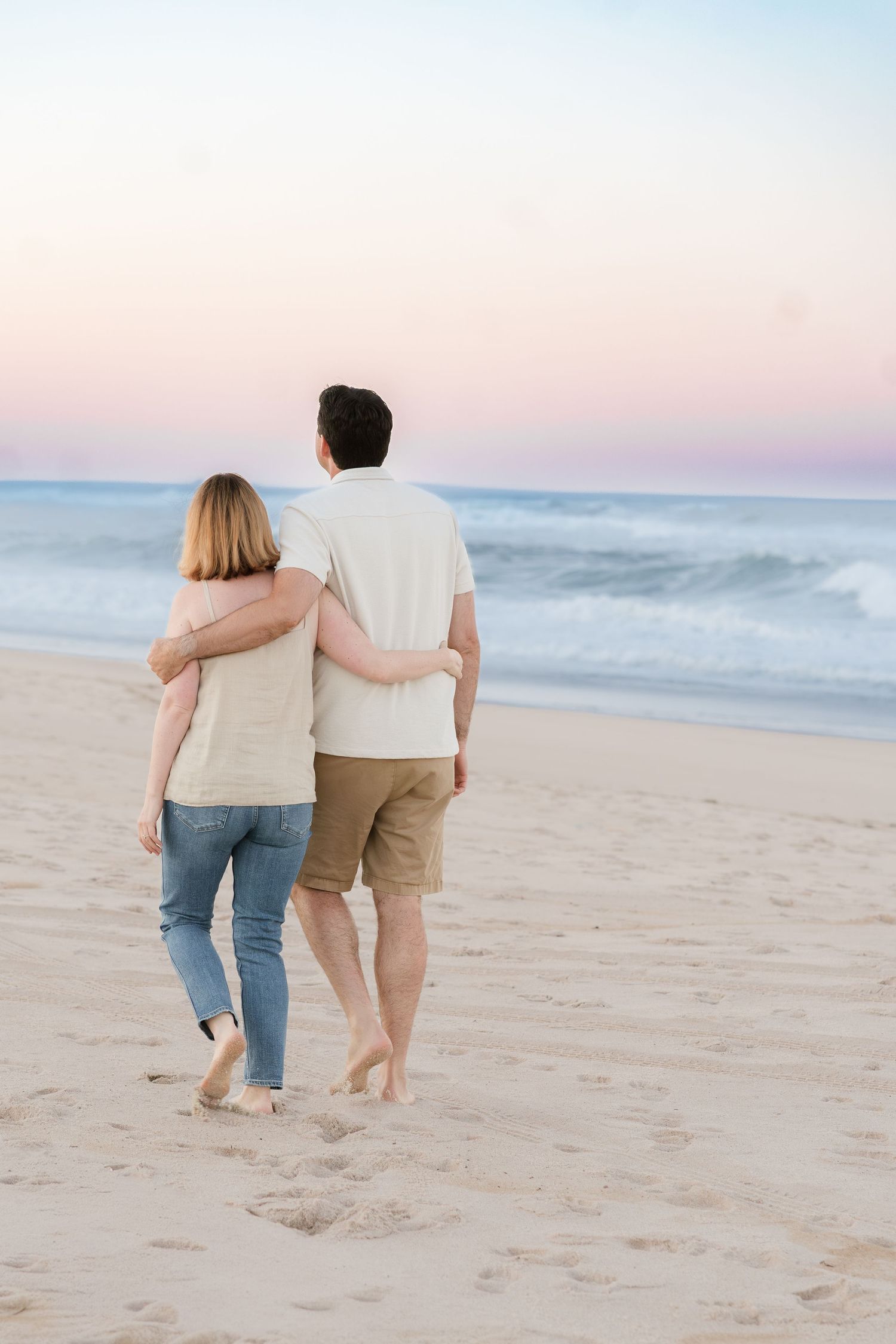 Two people walking together on sandy beach at sunset.