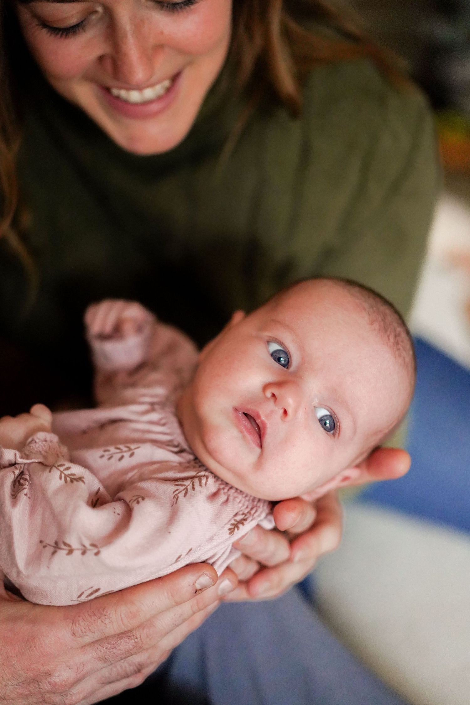 Baby in pink floral outfit looking up with bright blue eyes during tender moment.