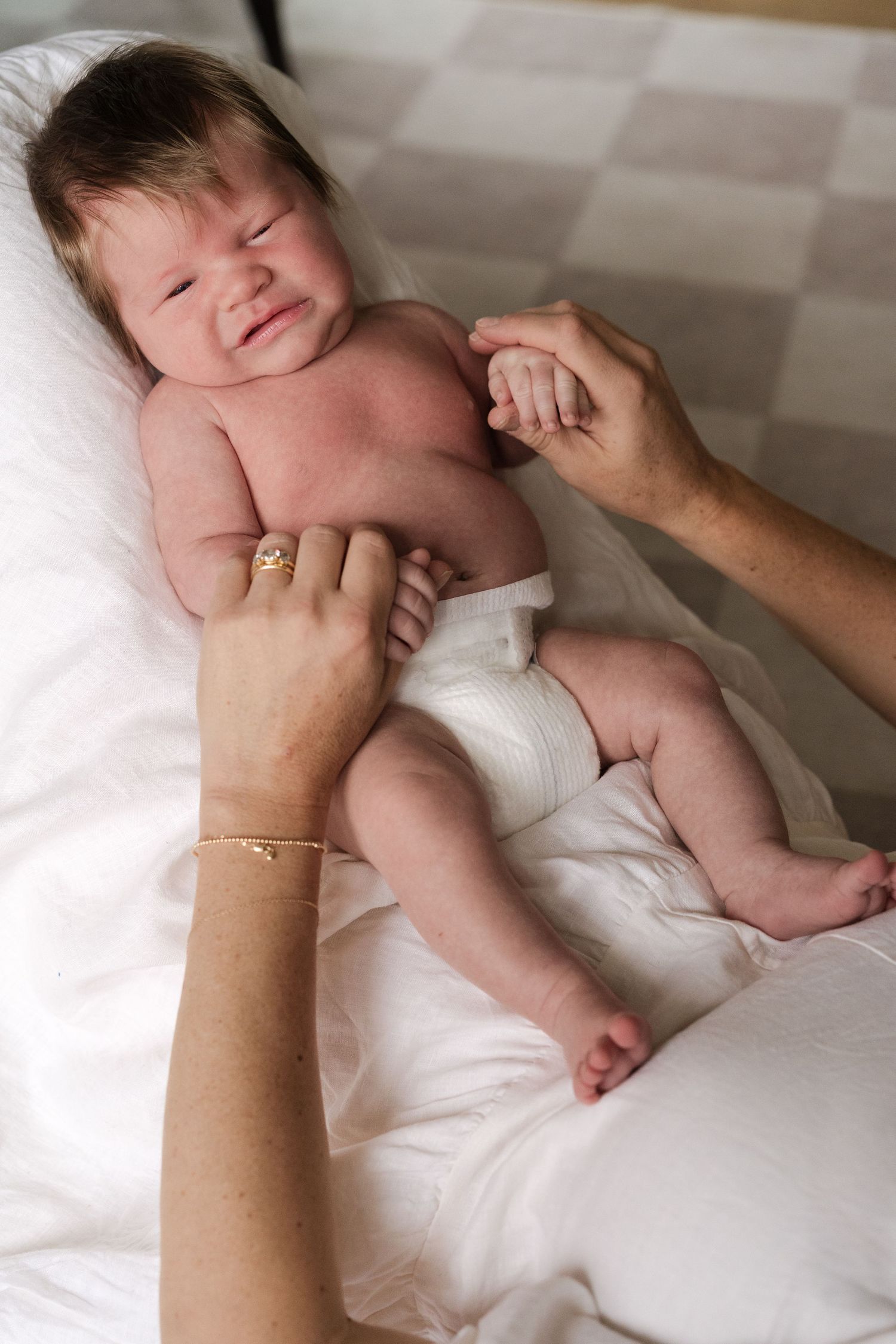 Series showing gentle interaction with a newborn baby on white bedding.