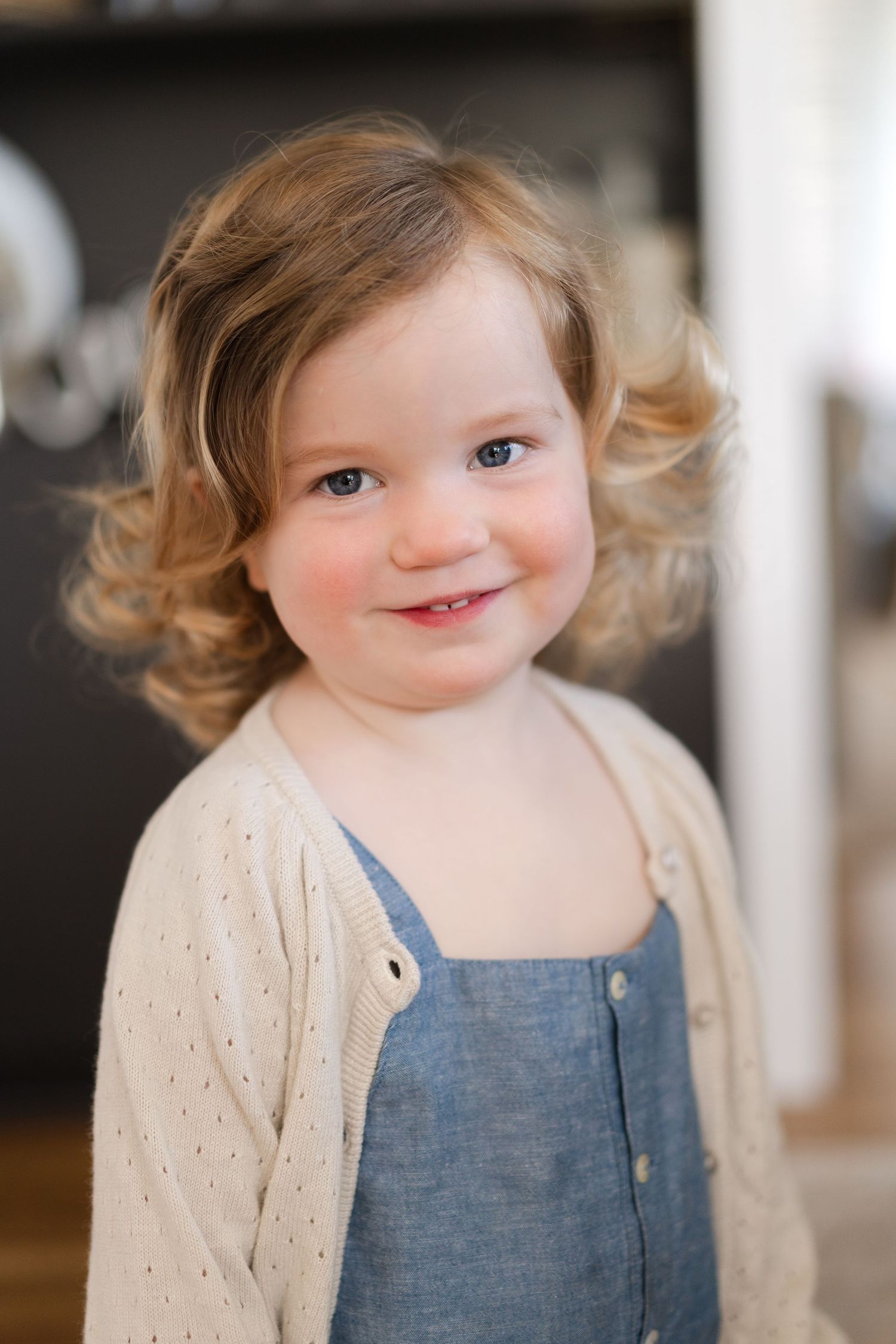 Close up portrait of toddler wearing blue denim overalls and cream cardigan.