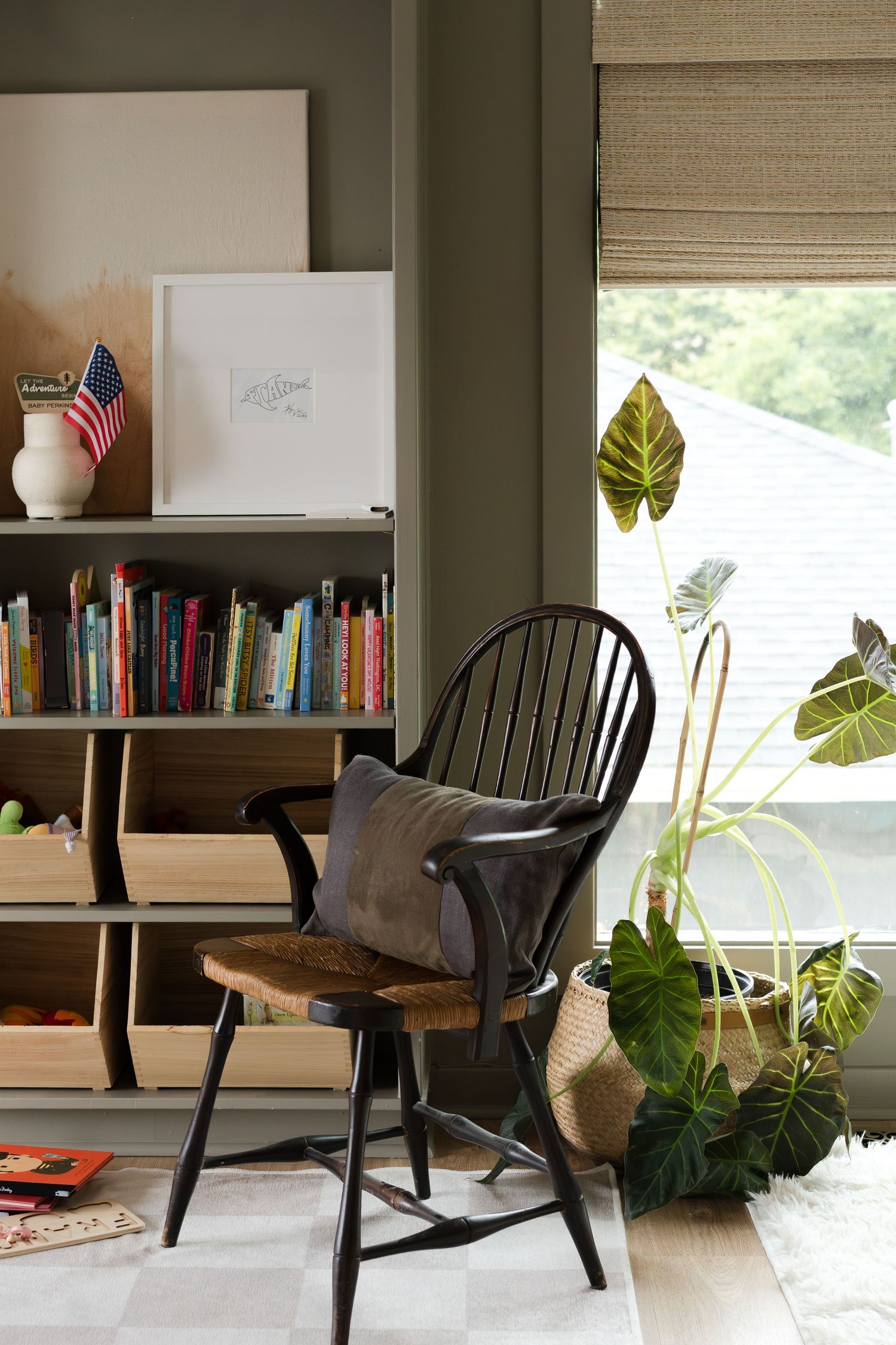 A cozy reading nook with Windsor chair, bookshelves, and tropical plants by the window.