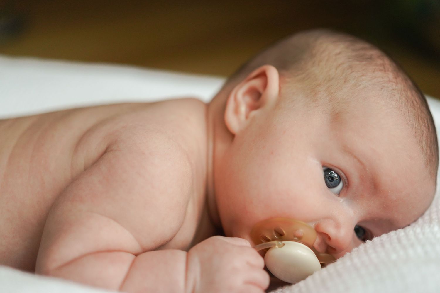 Close-up of an infant lying on white fabric with bright blue eyes.