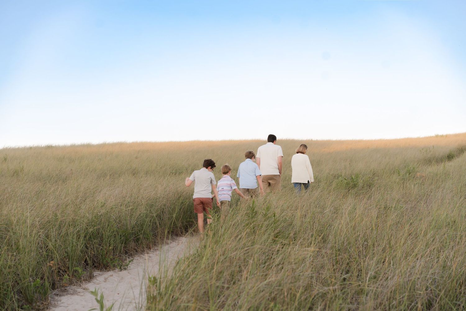 Distant view of a family walking through tall grass on a coastal path at sunset.