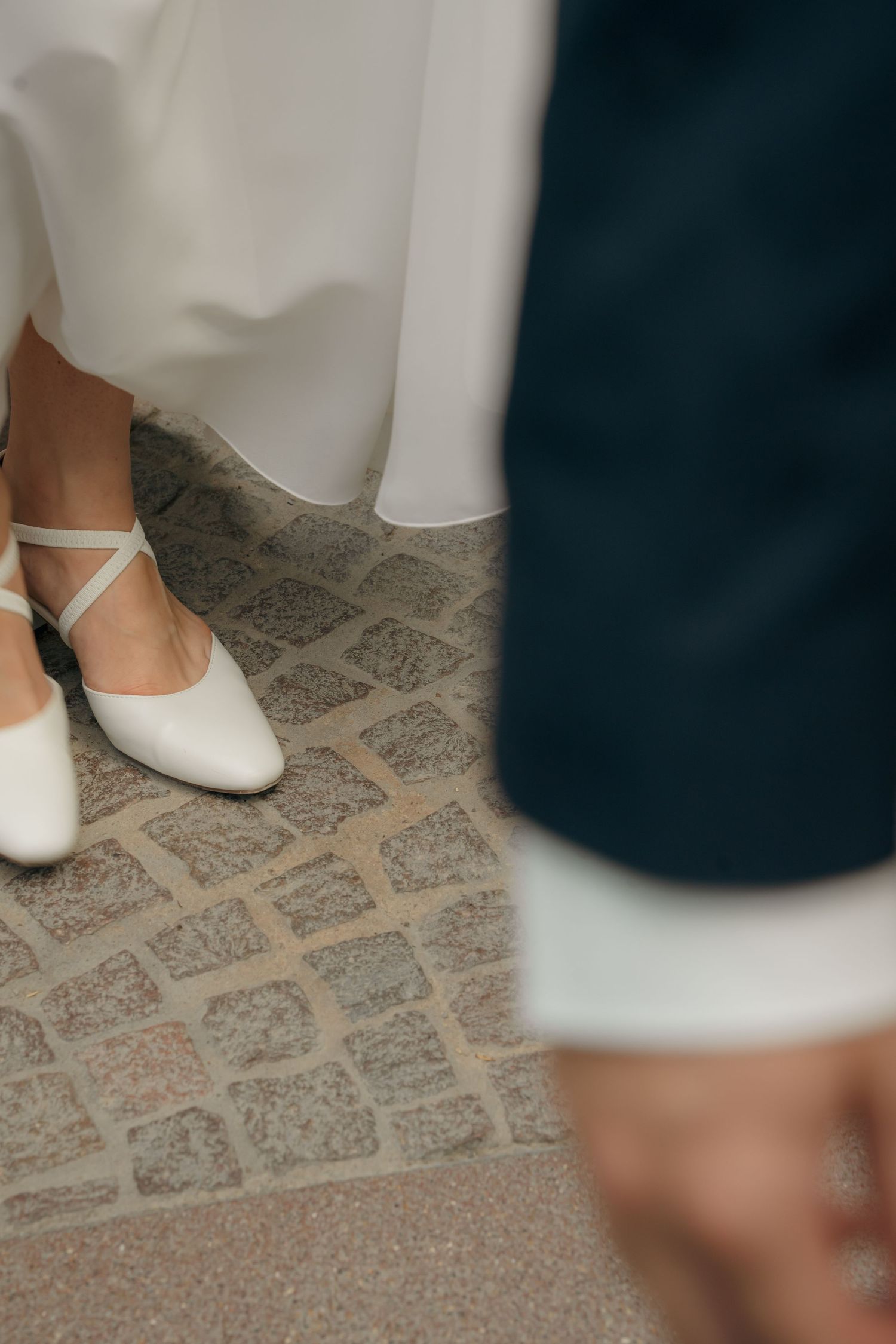 Braut steht im Hochzeitskleid vor dem Bräutigam, Detailaufnahme von Schuhen und Anzug beim First Look