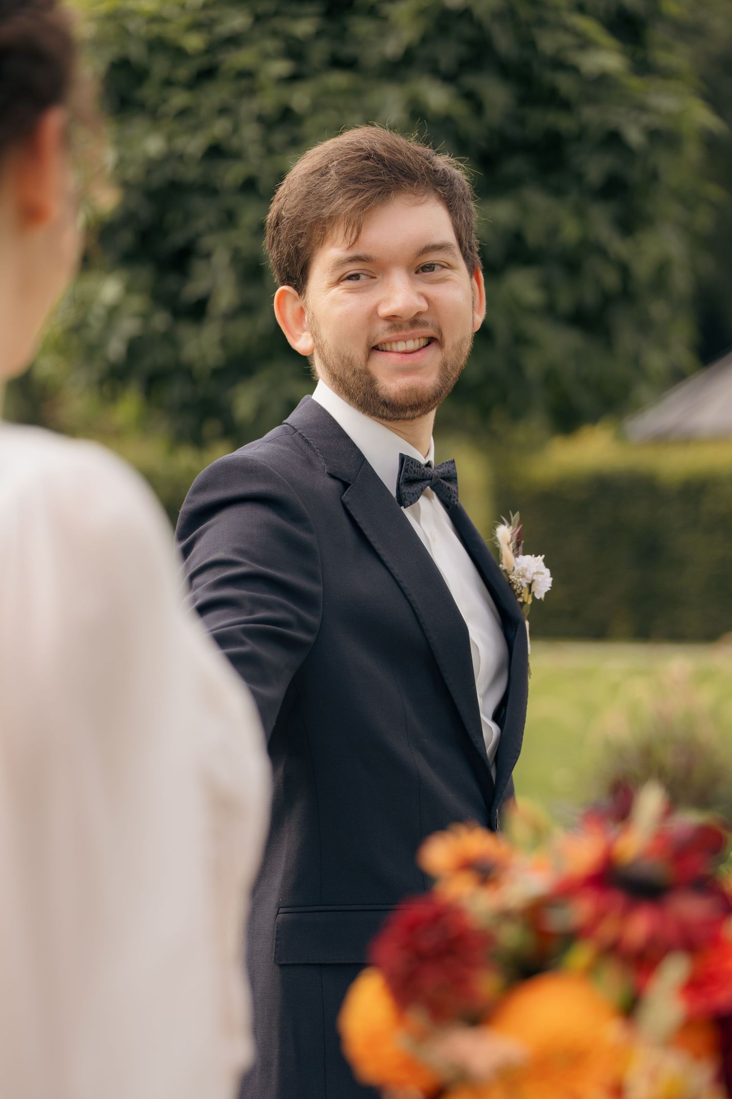 Bräutigam blickt lächelnd zur Braut, emotionales Hochzeitsporträt mit Blumenstrauß im Vordergrund
