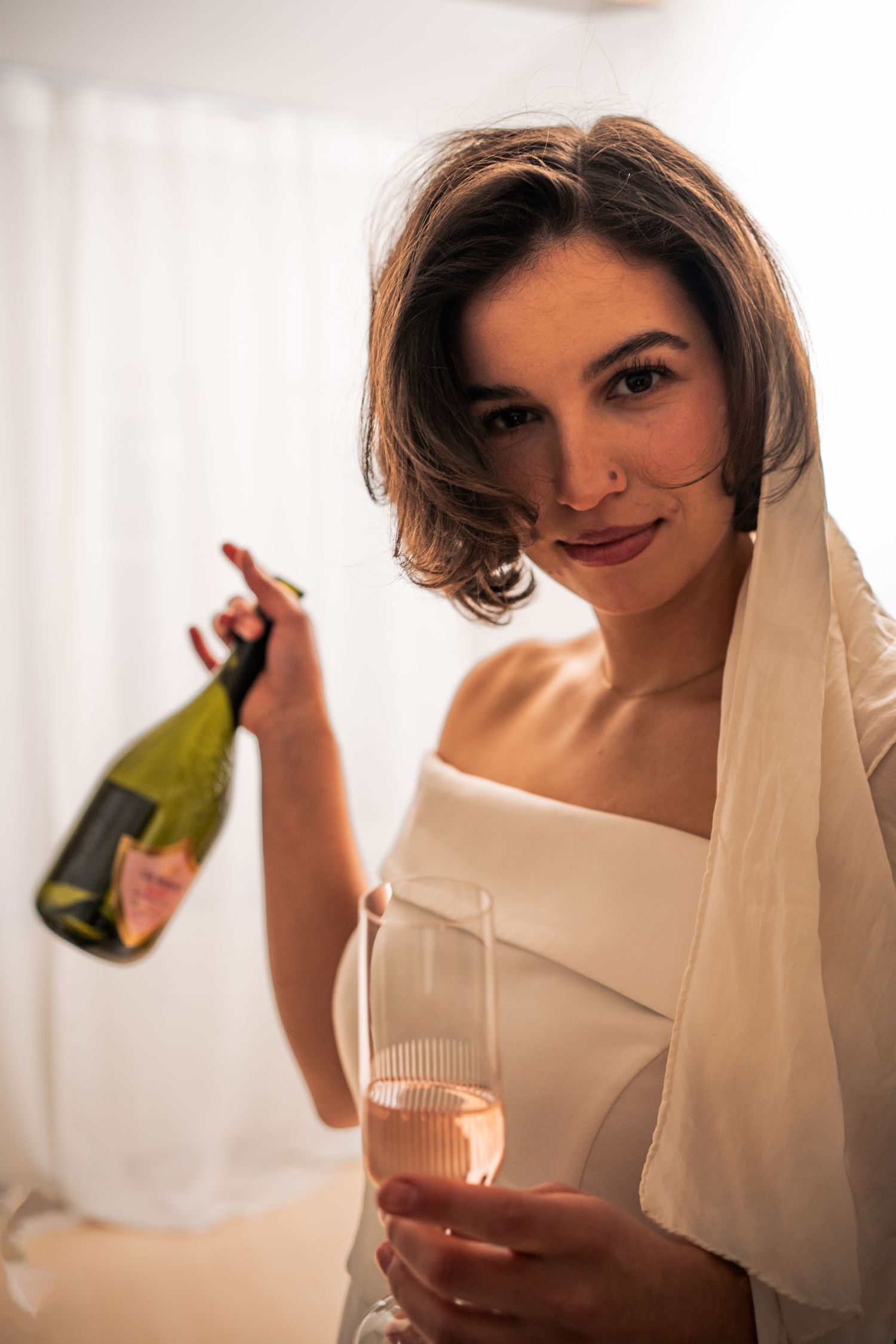 Braut blickt lächelnd in die Kamera, hält Sektglas und Flasche, modernes Brautporträt mit natürlicher Ausstrahlung