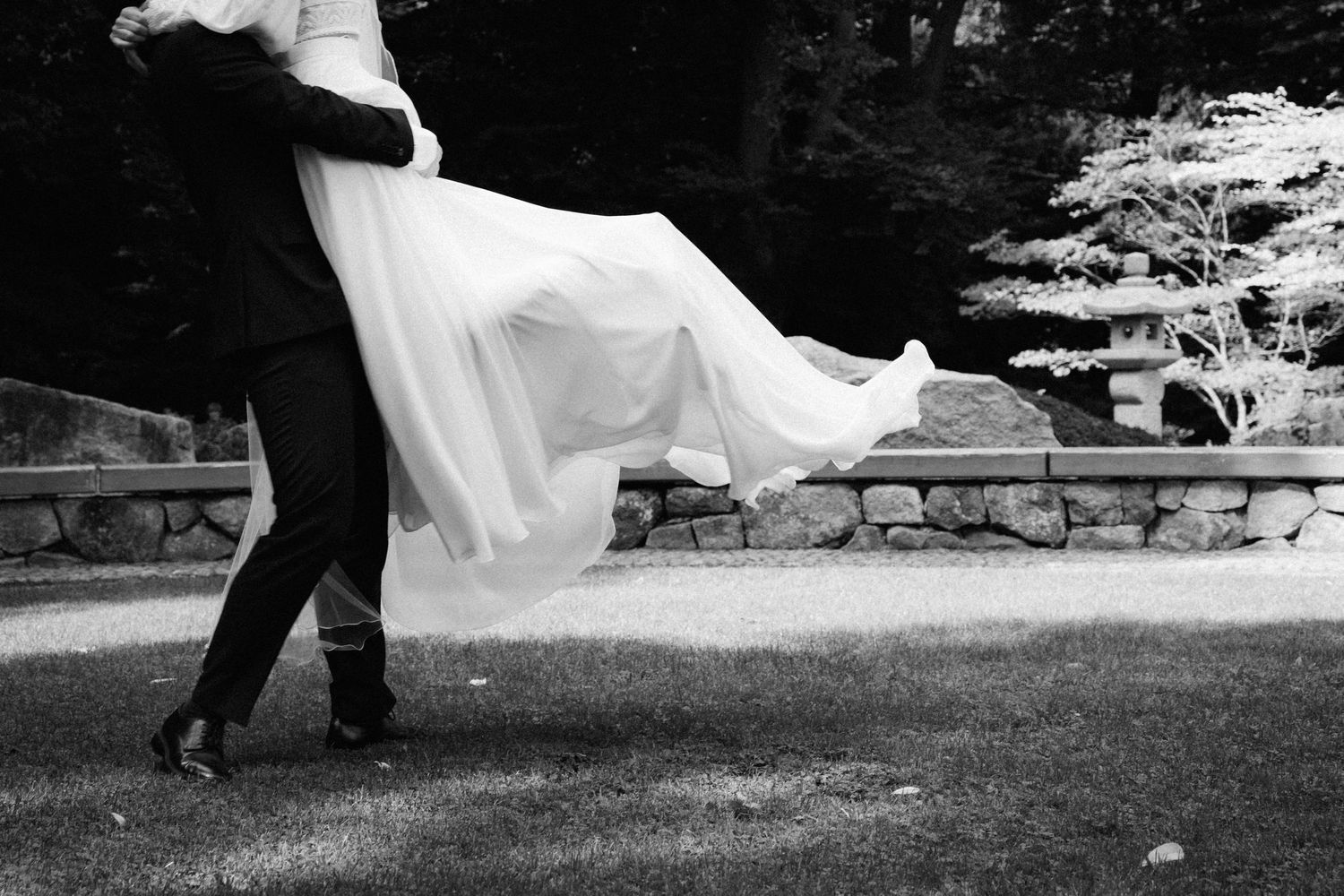 Schwarzweißaufnahme eines Brautpaares beim First Look, Brautkleid bewegt sich im Moment der Umarmung