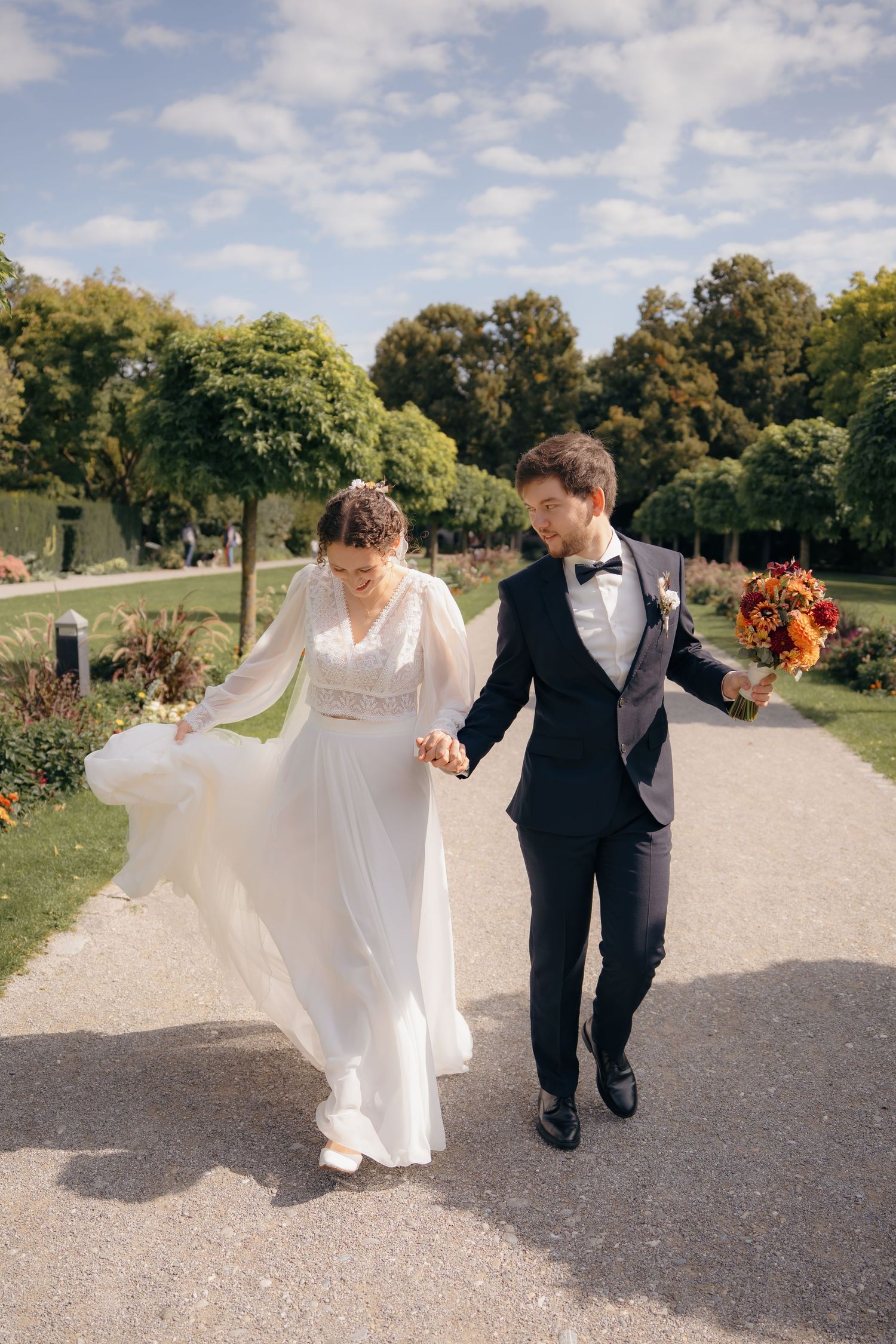 Brautpaar läuft Hand in Hand durch einen Park, Braut hält ihr Kleid, lebendige Hochzeitsfotografie im Freien