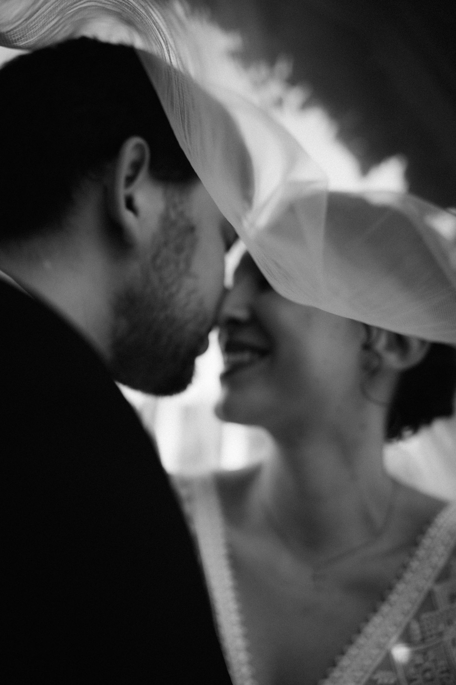 Schwarzweißporträt eines Brautpaares unter dem Schleier, intime und emotionale Hochzeitsfotografie