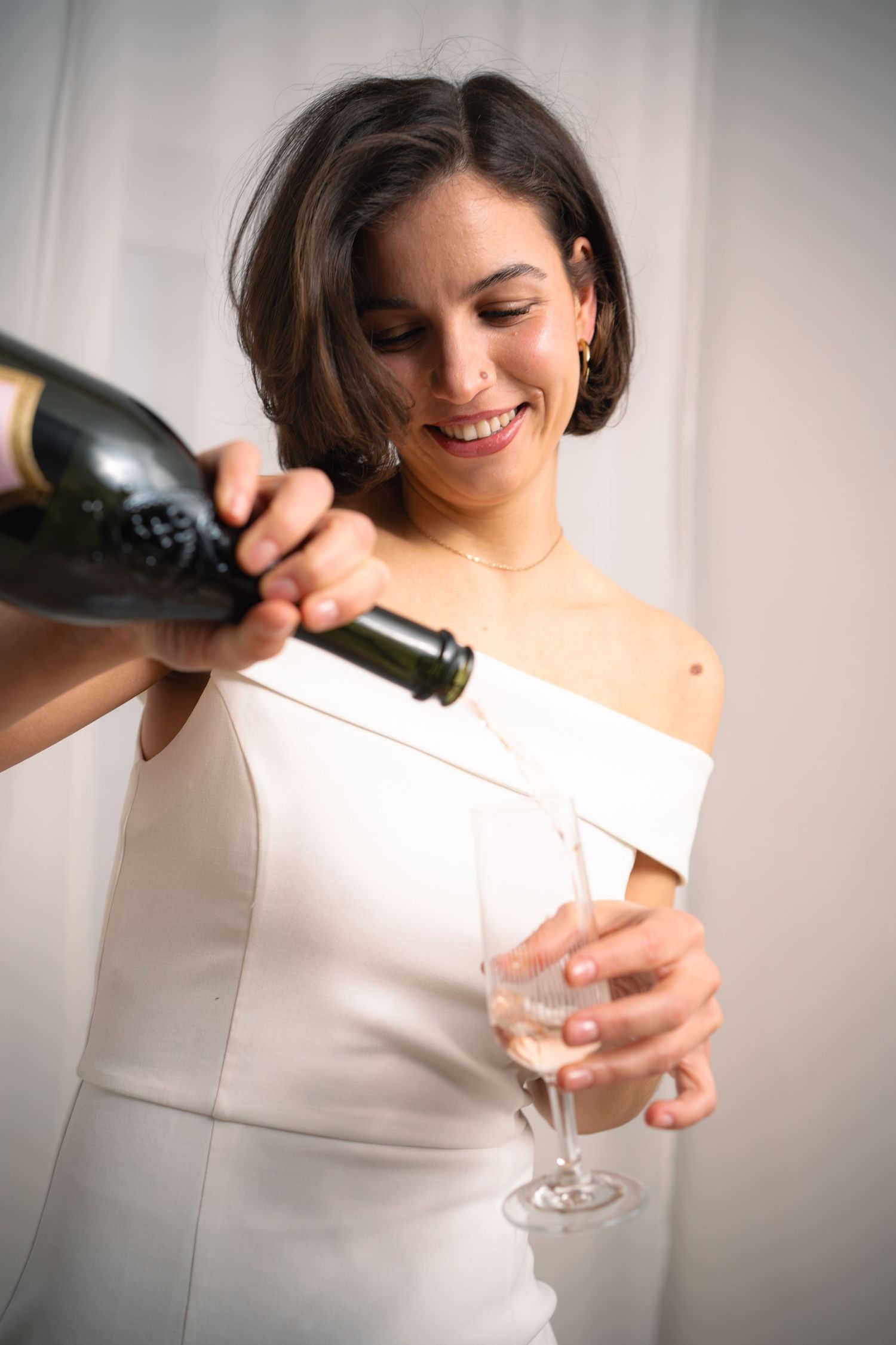 Braut im schlichten Brautkleid schenkt Sekt ein, natürliches Brautshooting mit weichem Licht im Innenraum