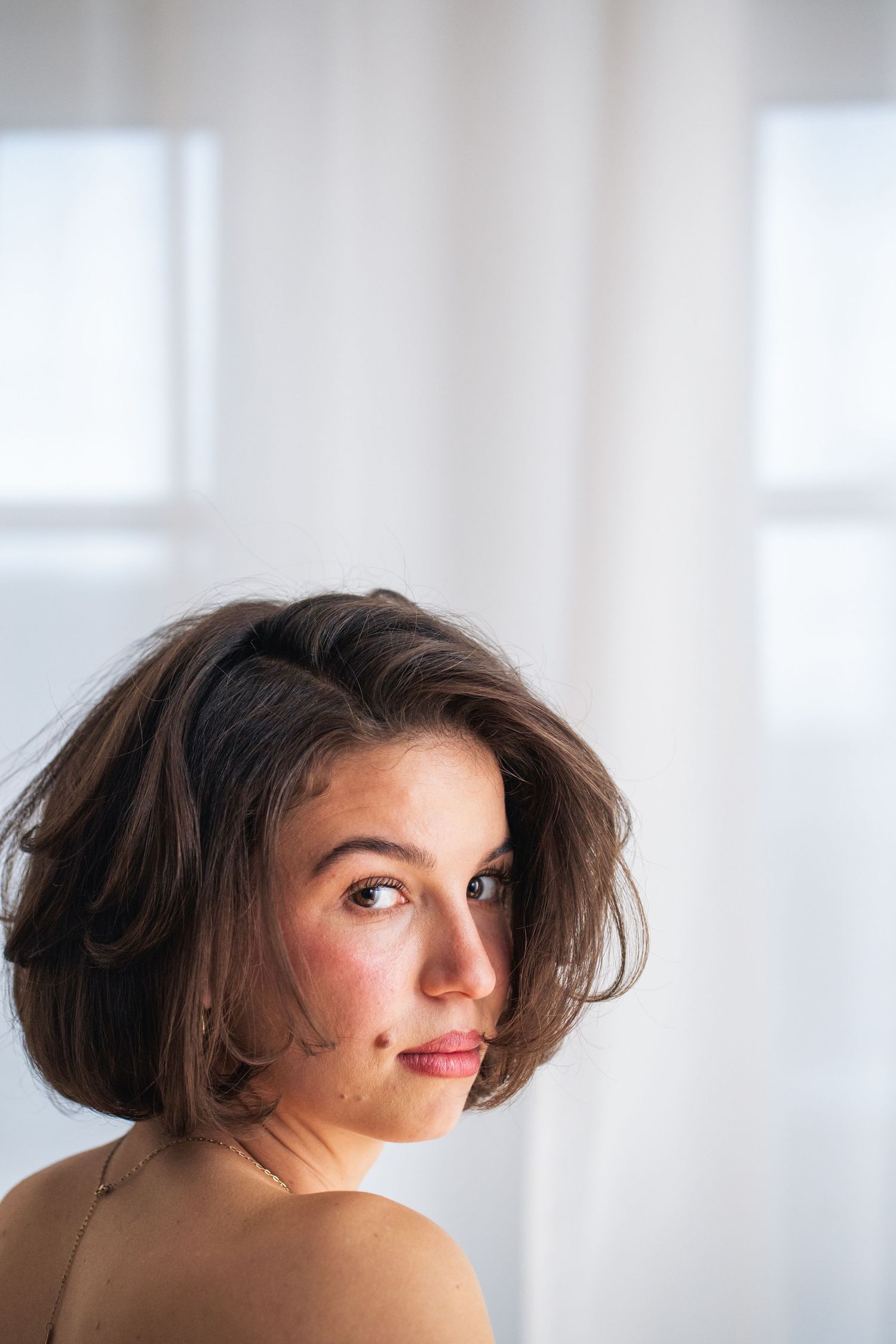 Nahes Porträt der Braut mit kurzem Haar, ruhiger Blick über die Schulter, modernes Brautshooting