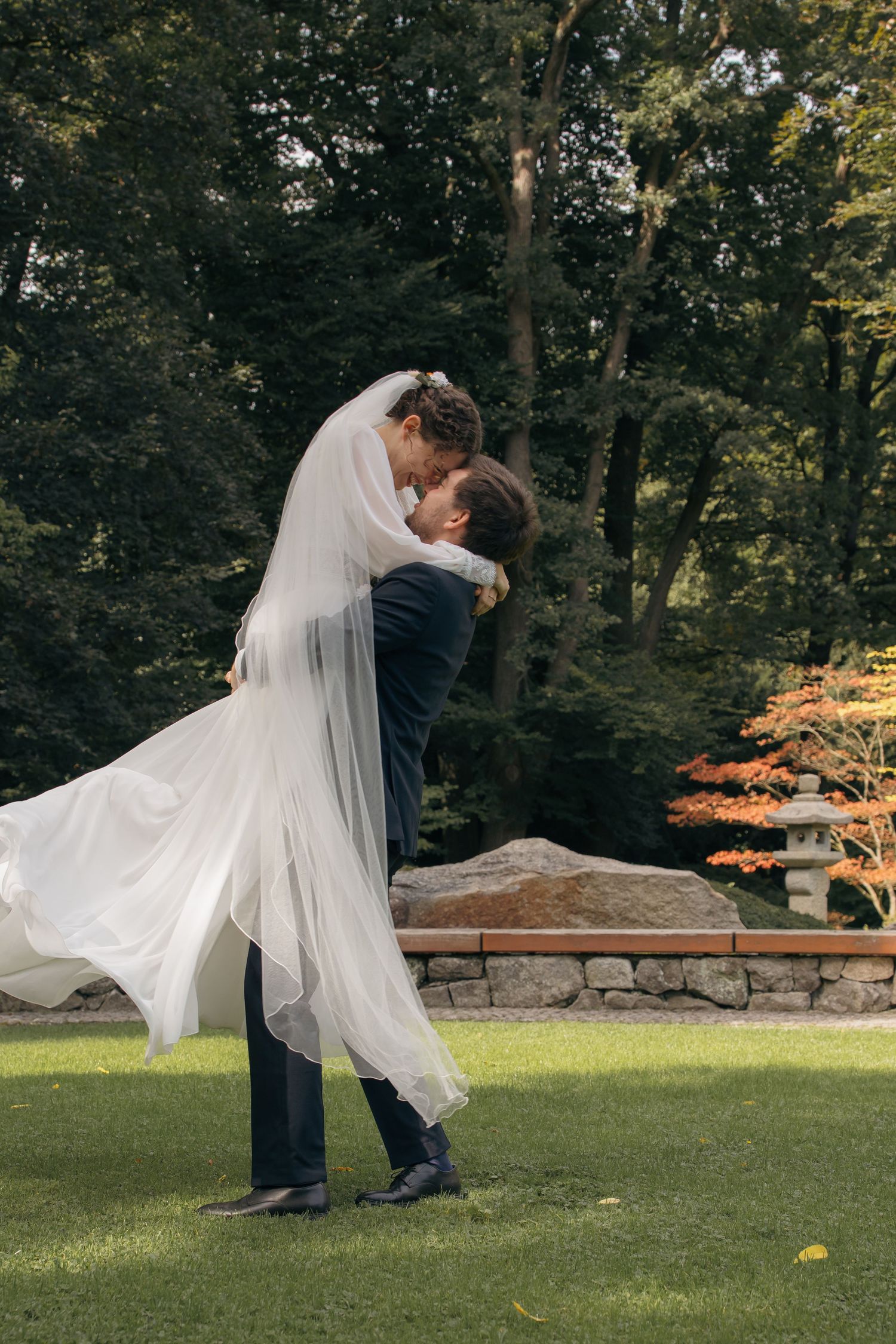 Bräutigam hebt die Braut im Hochzeitskleid hoch, emotionaler First Look im natürlichen Umfeld