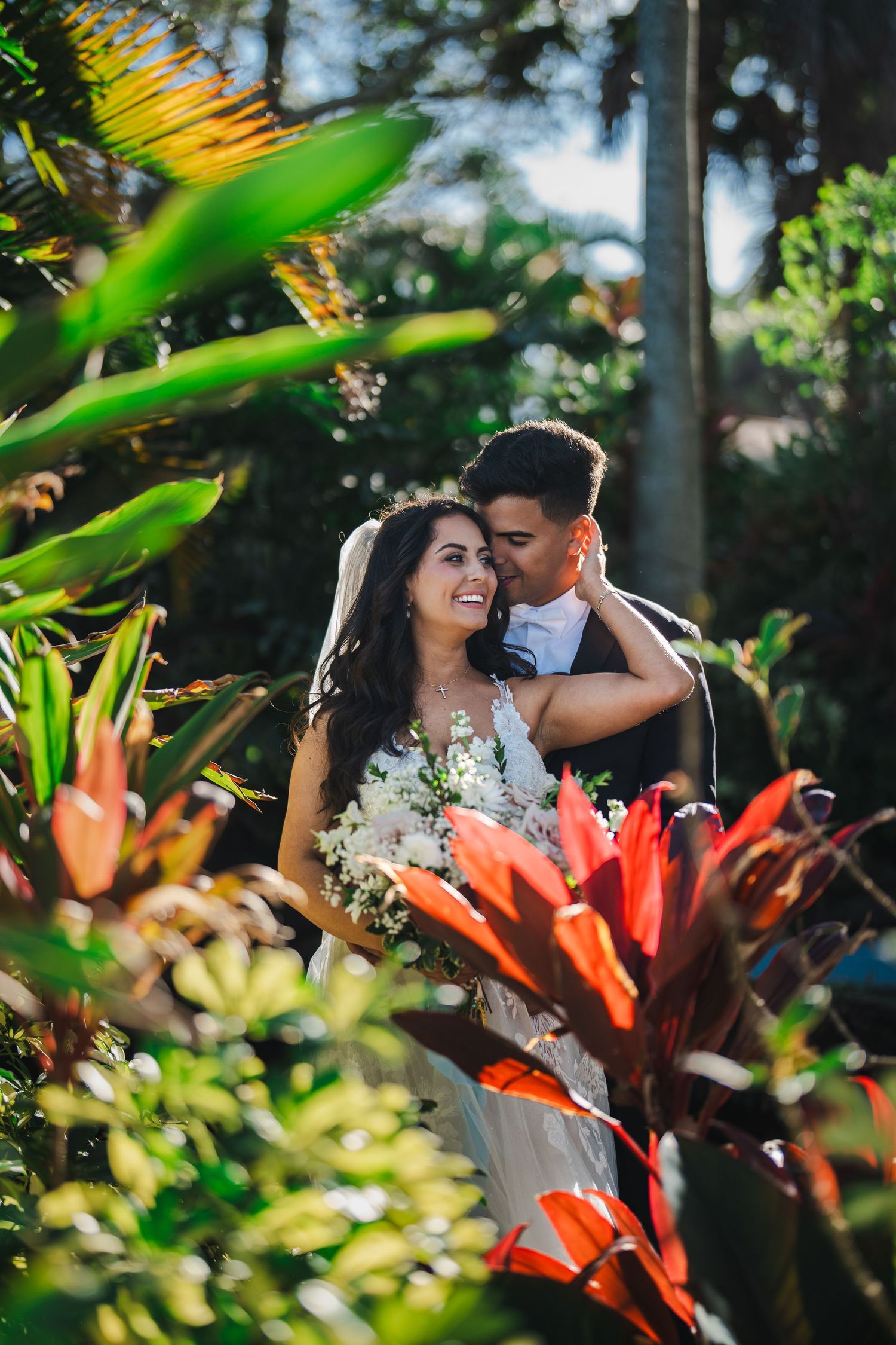 Romantic outdoor wedding portrait of bride and groom surrounded by lush tropical greenery and vibrant plants in Florida, featuring natural s