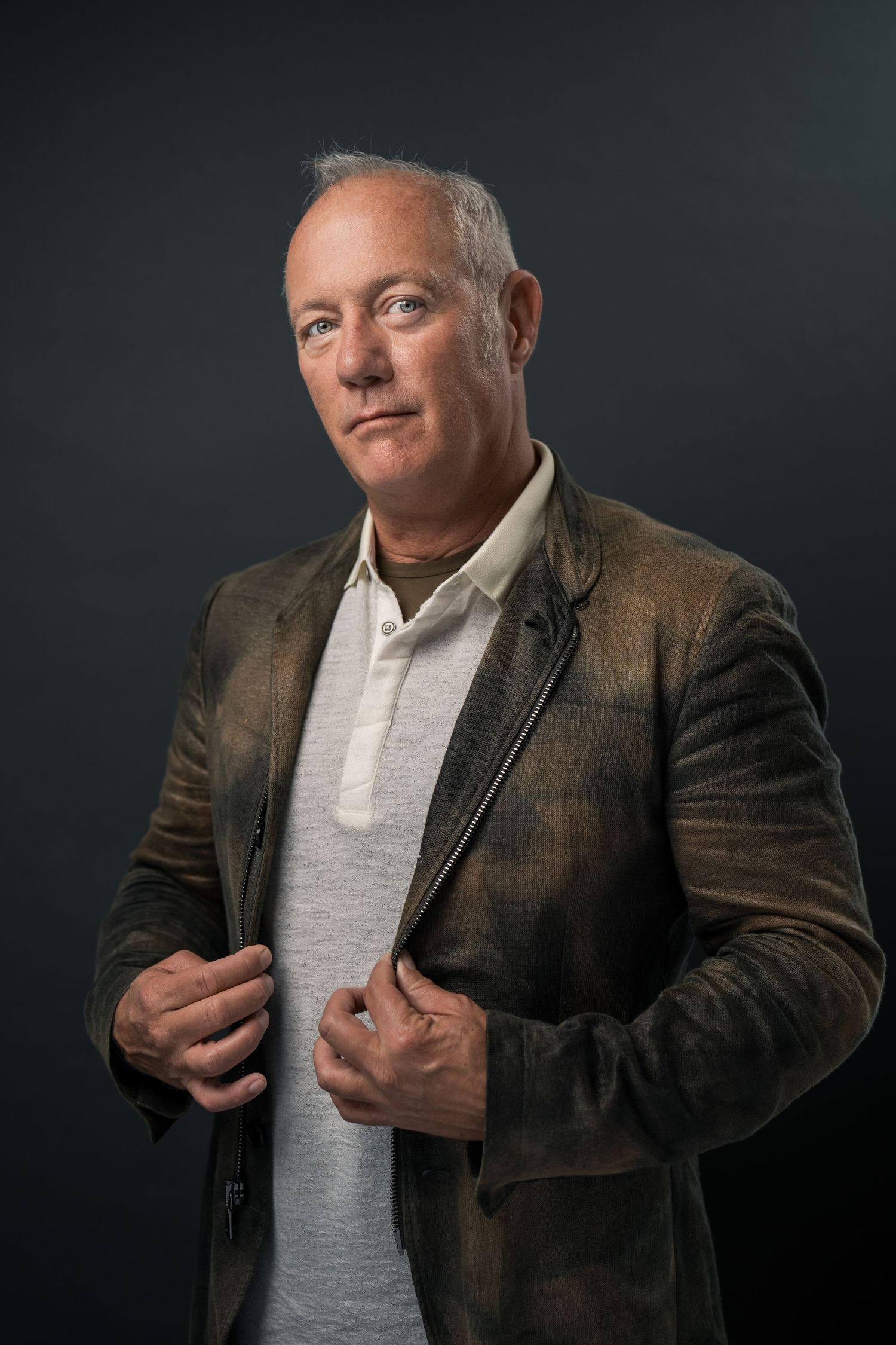 Professional corporate headshot of a confident businessman wearing a modern textured jacket against a dark studio background, captured with