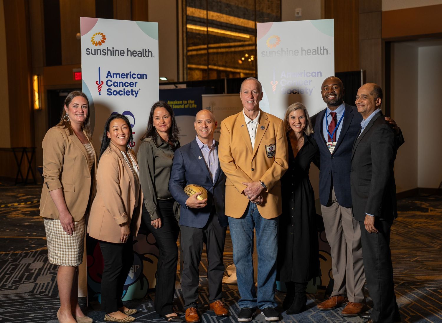 Group of professionals posing together at Sunshine Health and American Cancer Society event in a ballroom.