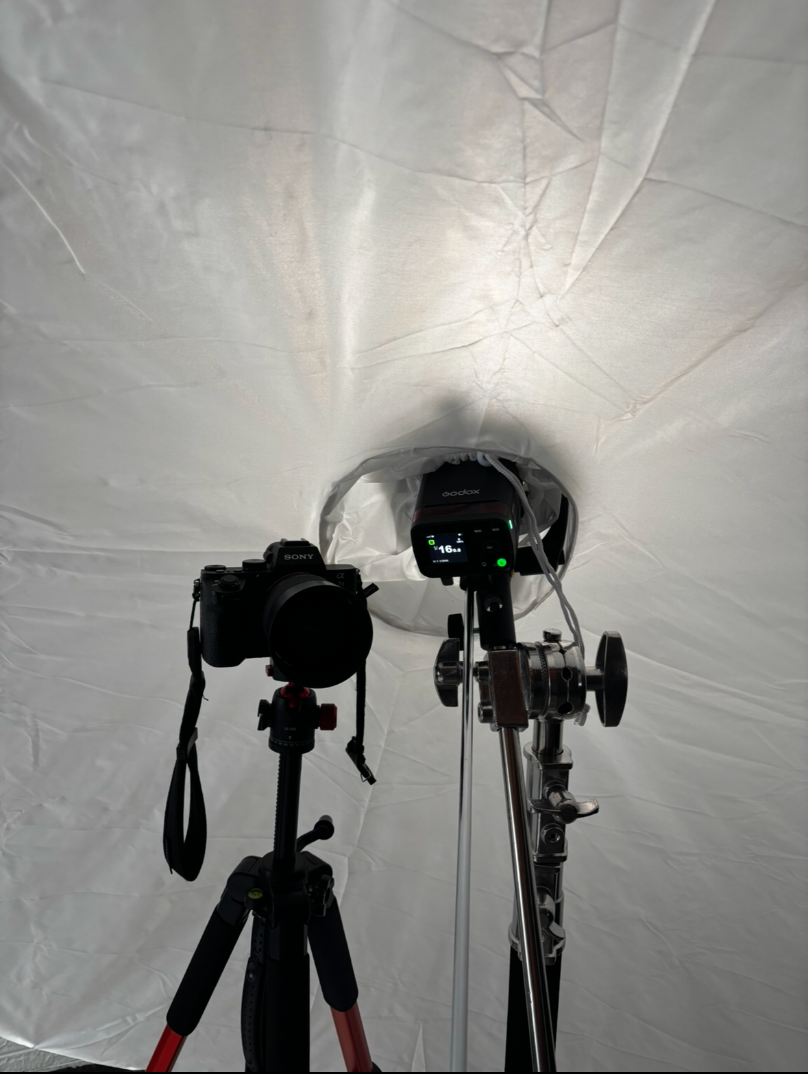 Camera and studio lighting equipment set up on tripods against a plain wall.