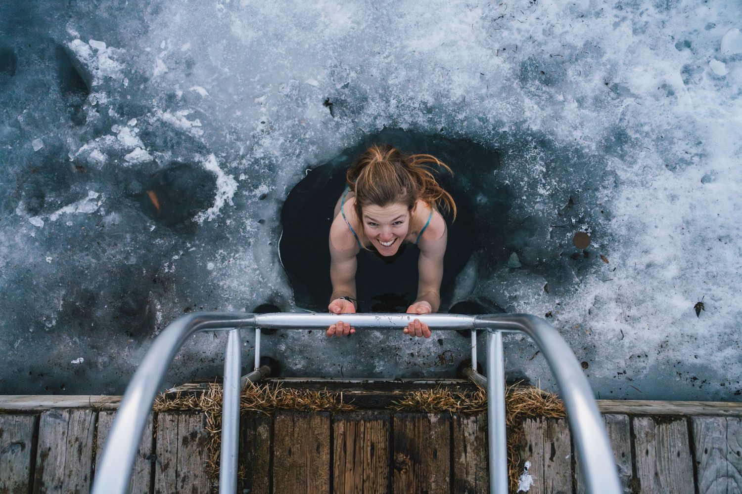 Woman climbing out of a frozen ice hole using a metal ladder in winter.