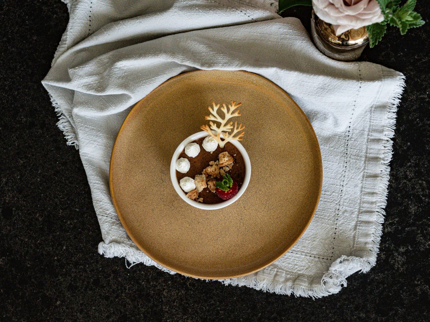 Elegant dessert with marshmallows and gold antler decoration served in a bowl on a rustic ceramic plate.