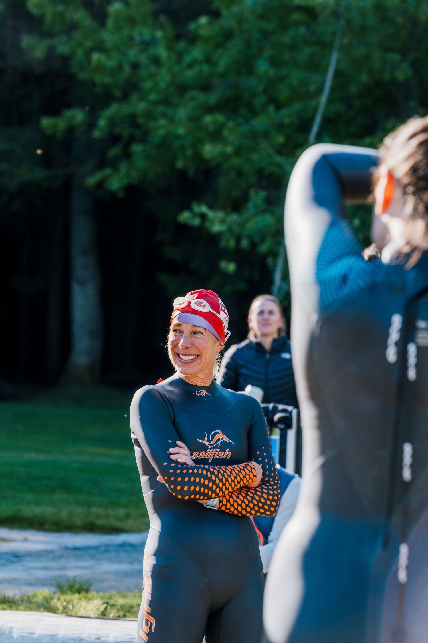 Female triathlete in Sailfish wetsuit and red swim cap smiling before a race outdoors.
