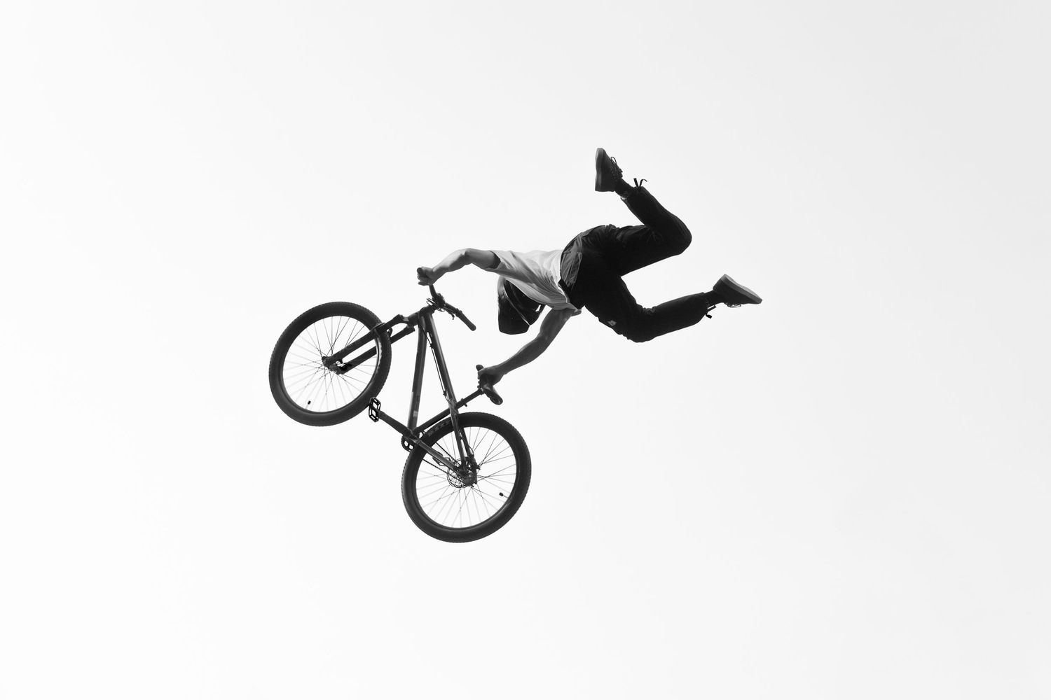 Black and white photo of a mountain biker performing a dramatic no-footer trick high in the air.