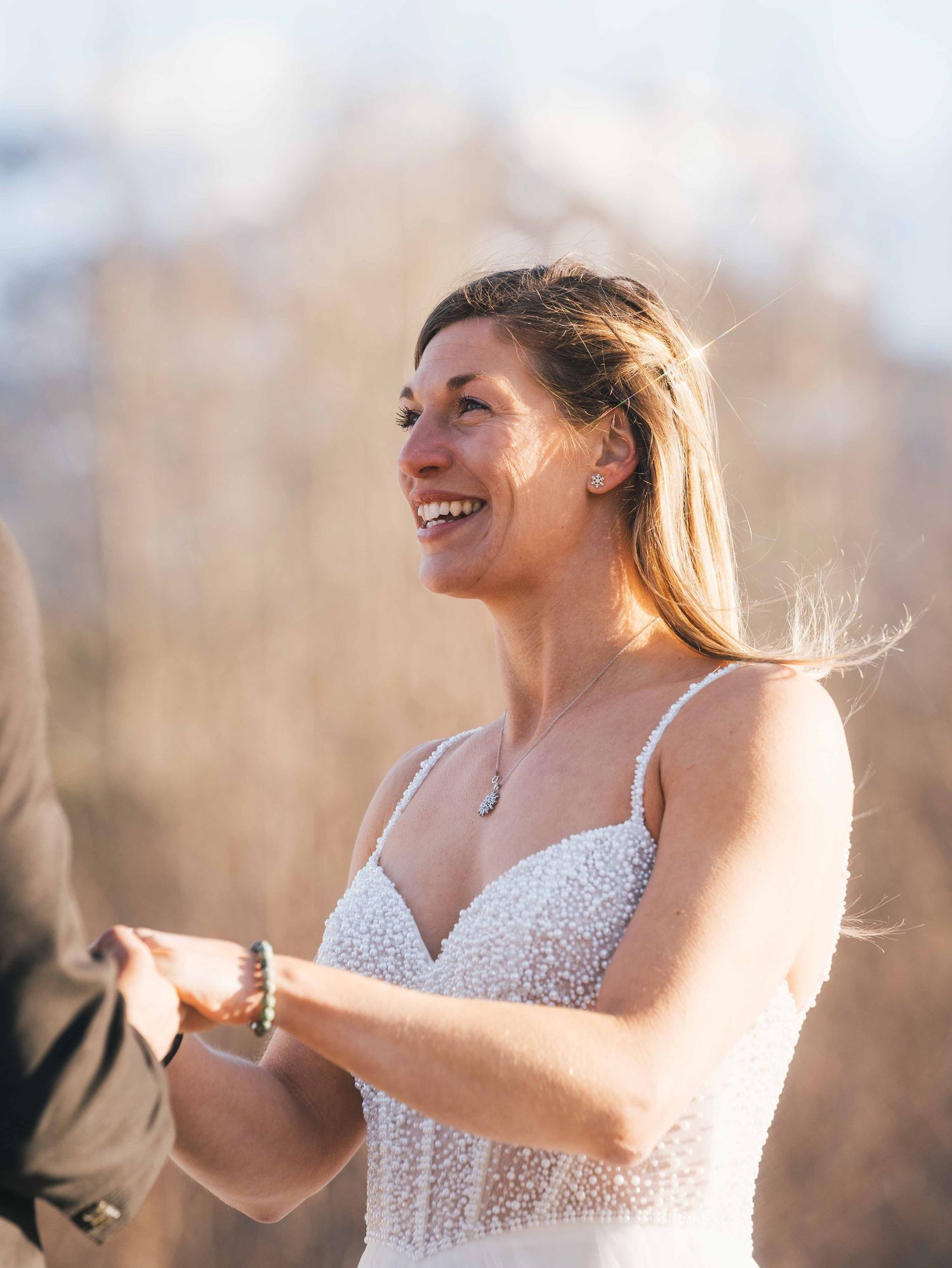 Radiant bride in beaded wedding gown smiling joyfully during an outdoor winter wedding ceremony.