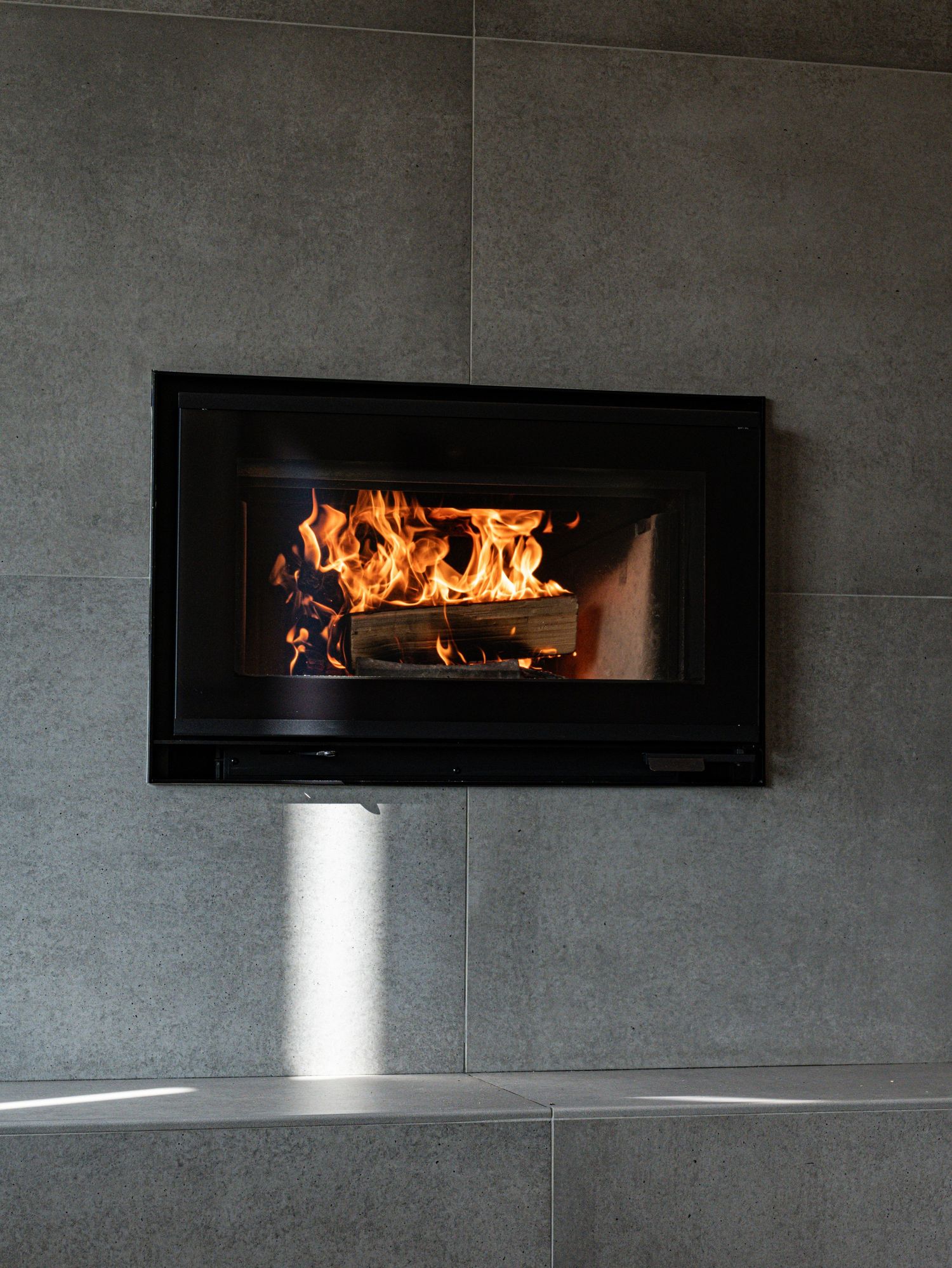 Modern built-in wood burning fireplace with flames in grey tiled wall.