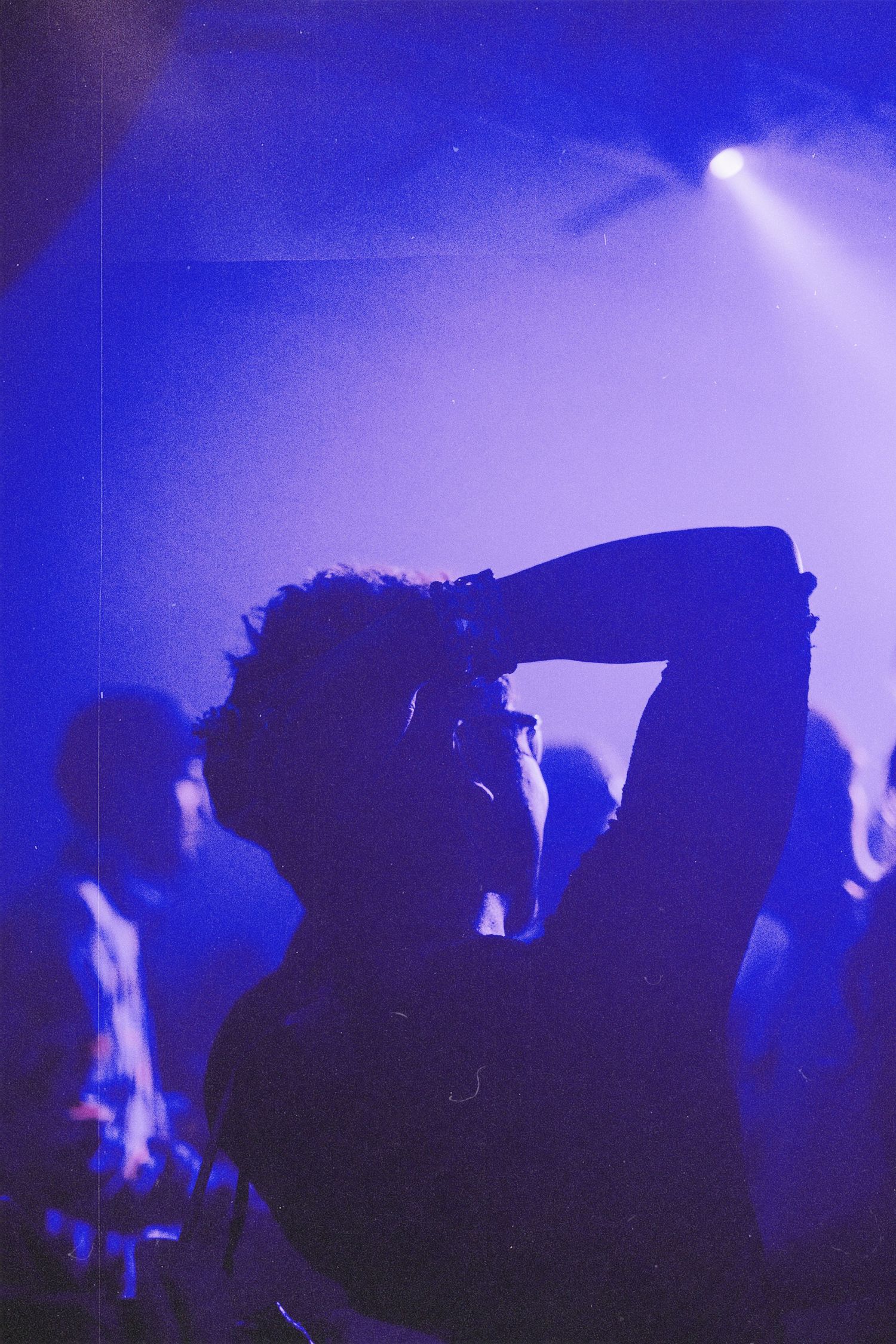 Silhouette of person drinking from bottle under blue stage lights at a live music event.