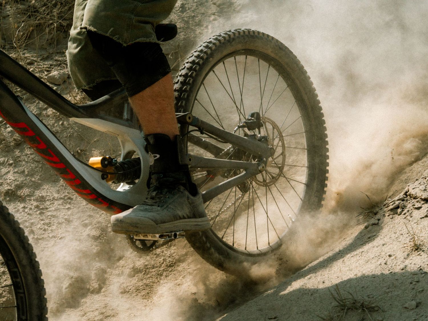 Mountain biker riding through dusty trail kicking up dirt cloud on rugged terrain.