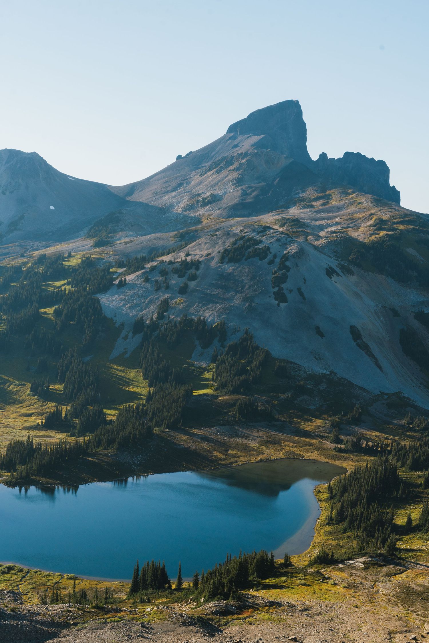 Stunning alpine lake reflecting blue sky beneath rocky mountain peak surrounded by evergreen trees.