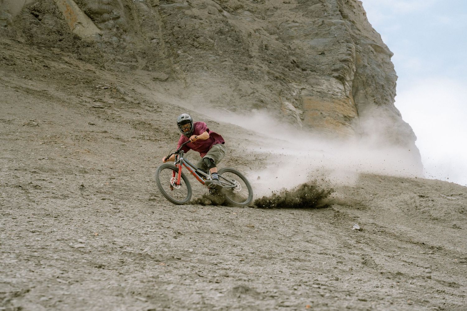Mountain biker carving through dusty terrain on a rocky hillside, sending clouds of dust into the air.