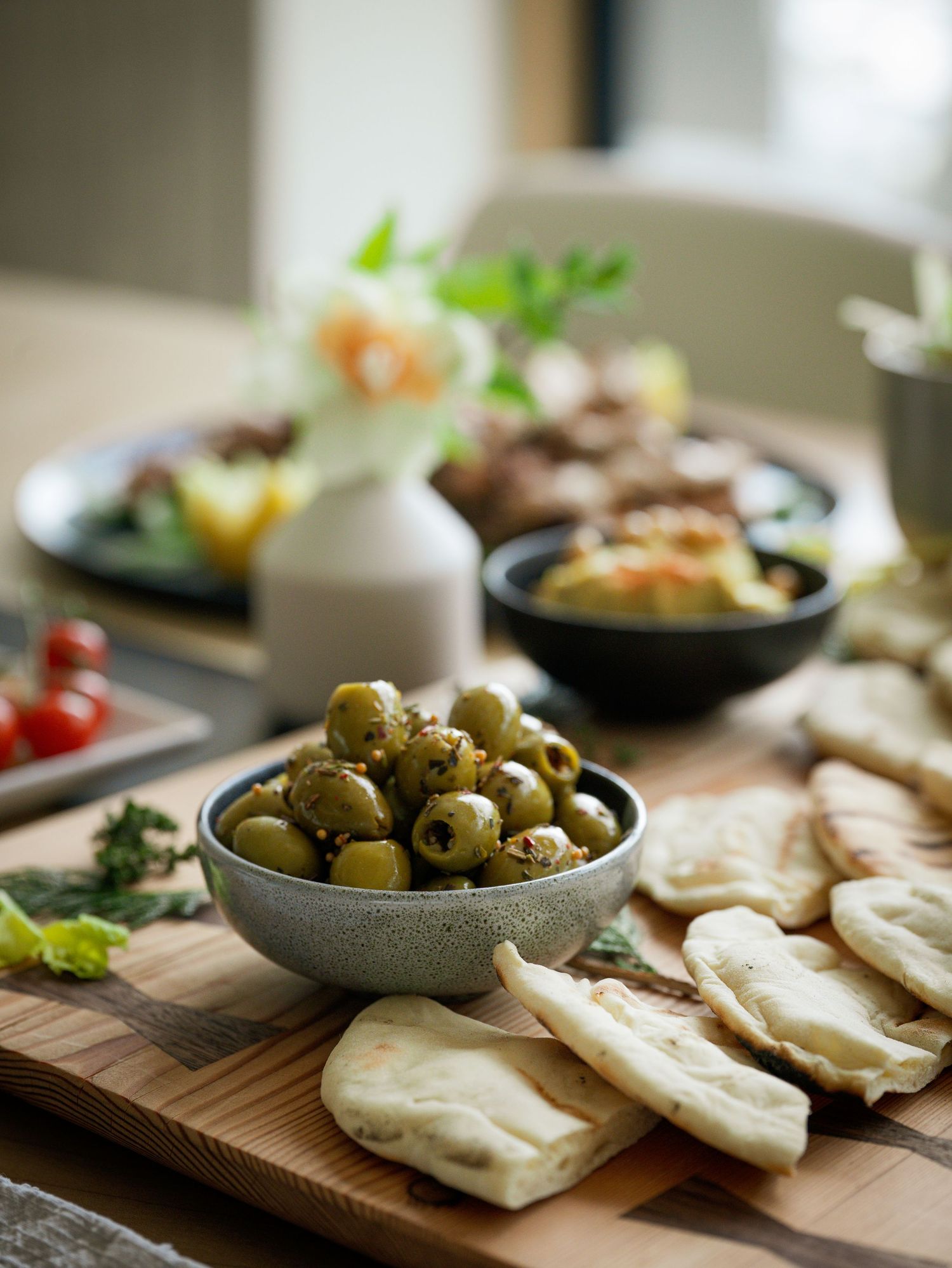 Rustic spread of green olives, flatbread, and Mediterranean dishes on a wooden serving board.