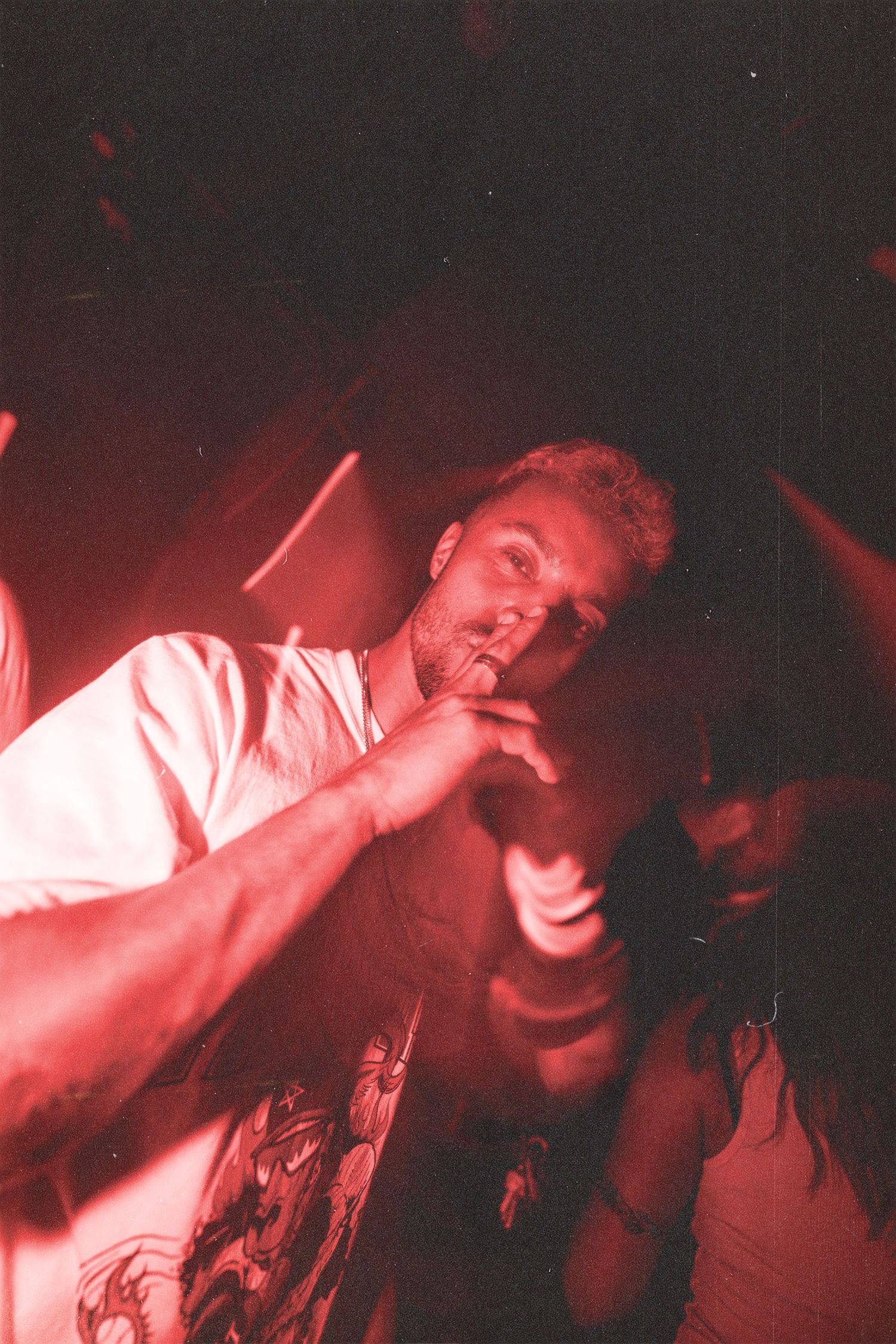 Man smoking a cigarette under dramatic red lighting at a dark nightclub, shot on film camera.
