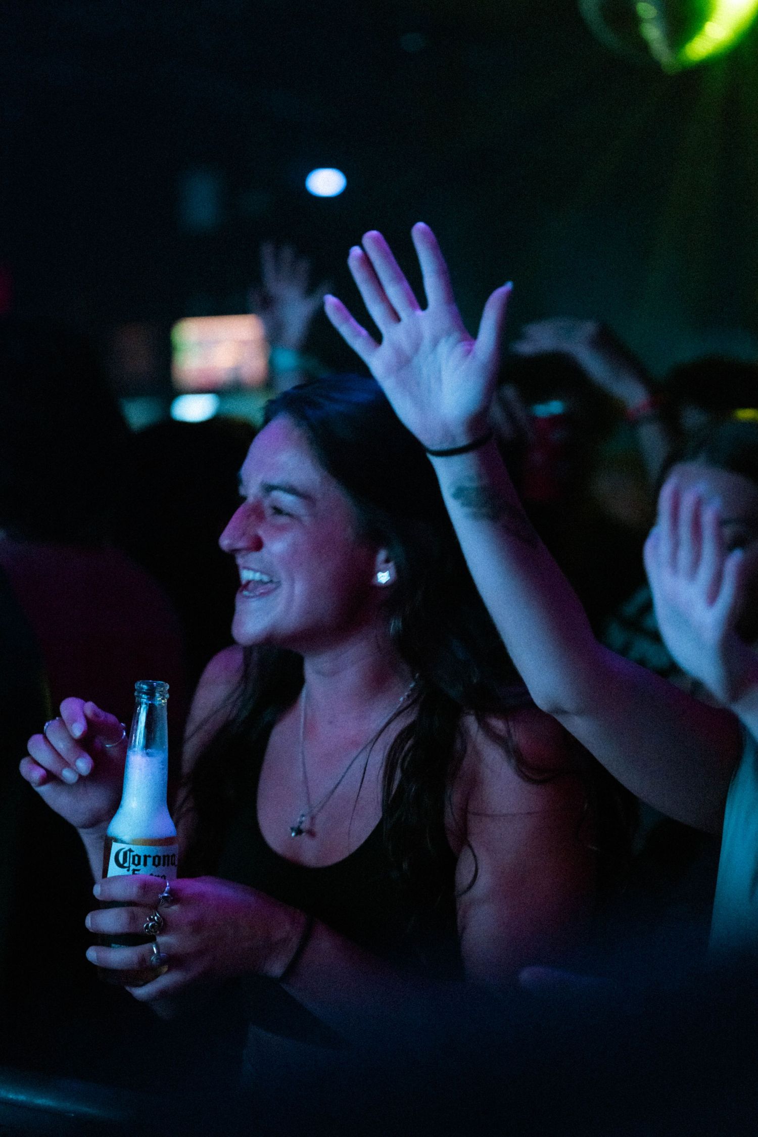 Happy woman holding Corona beer with hand raised at a vibrant nightclub concert.