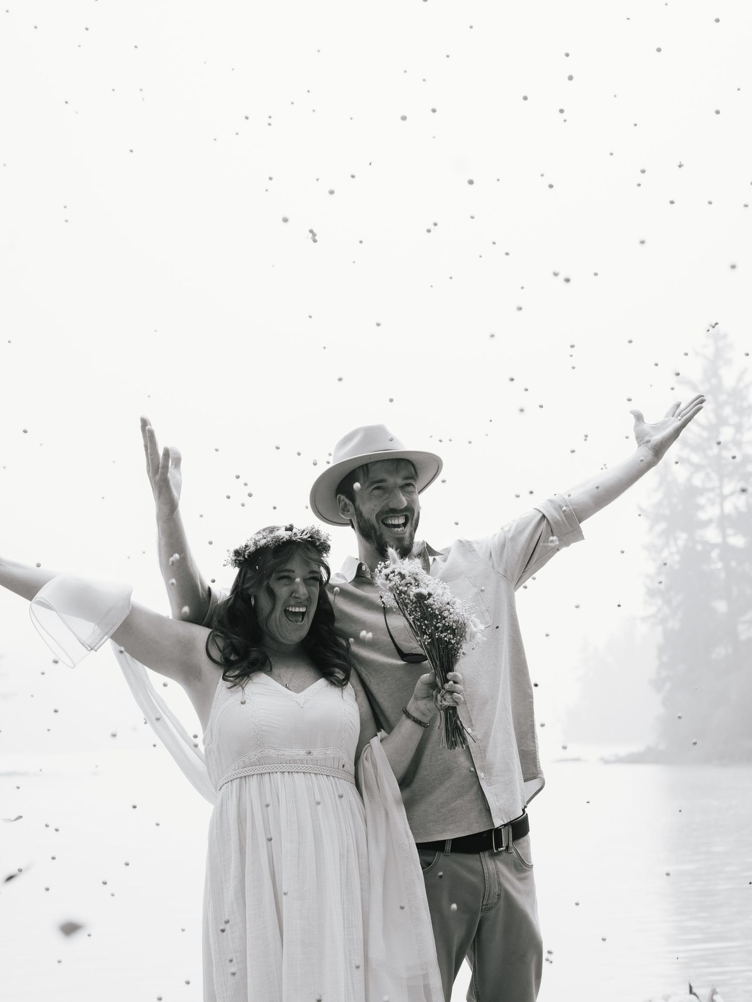 Joyful newlywed couple celebrating with confetti in a black and white wedding photograph.